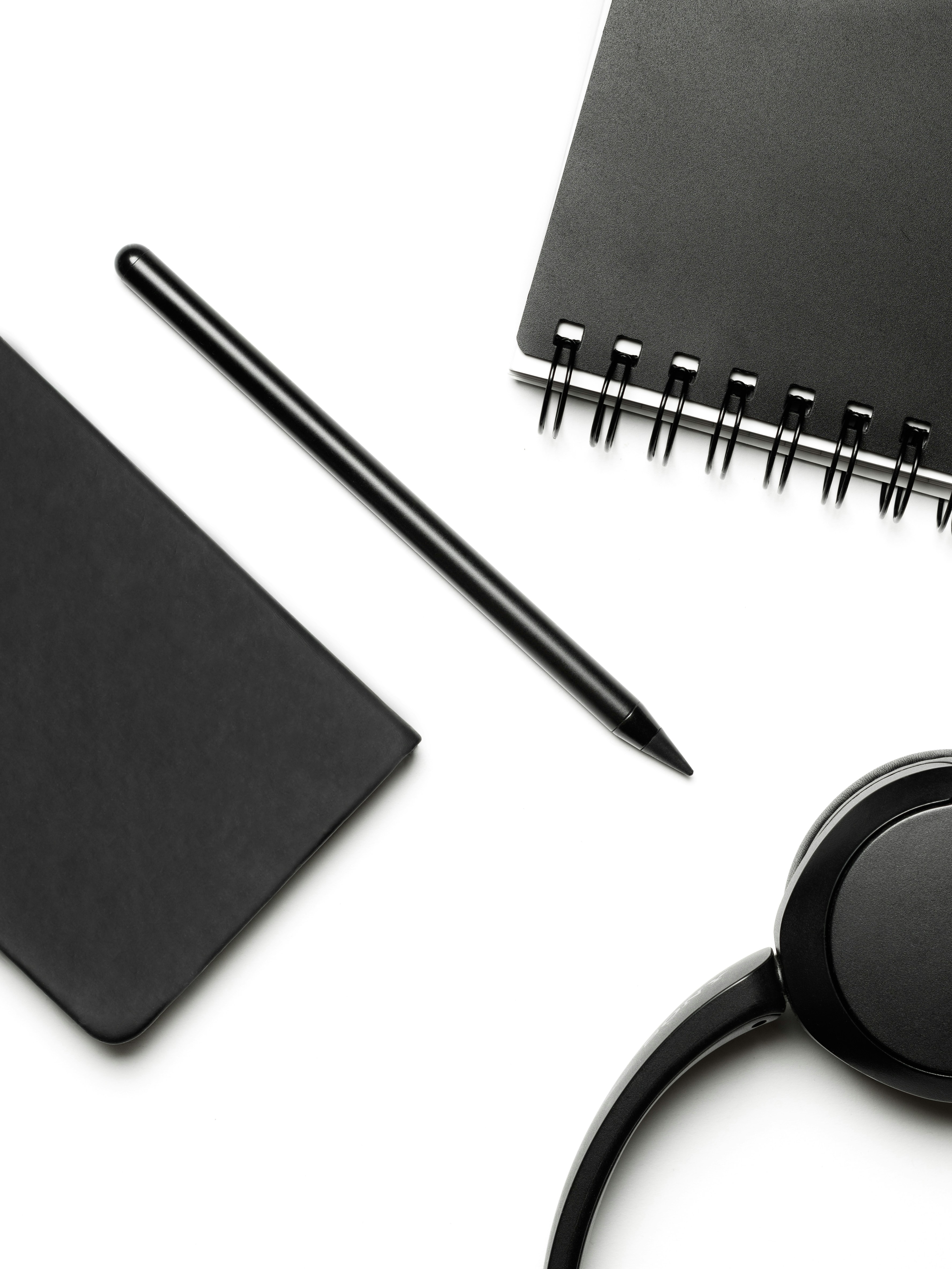 白い表面に黒のノート、ペン、ヘッドフォン。