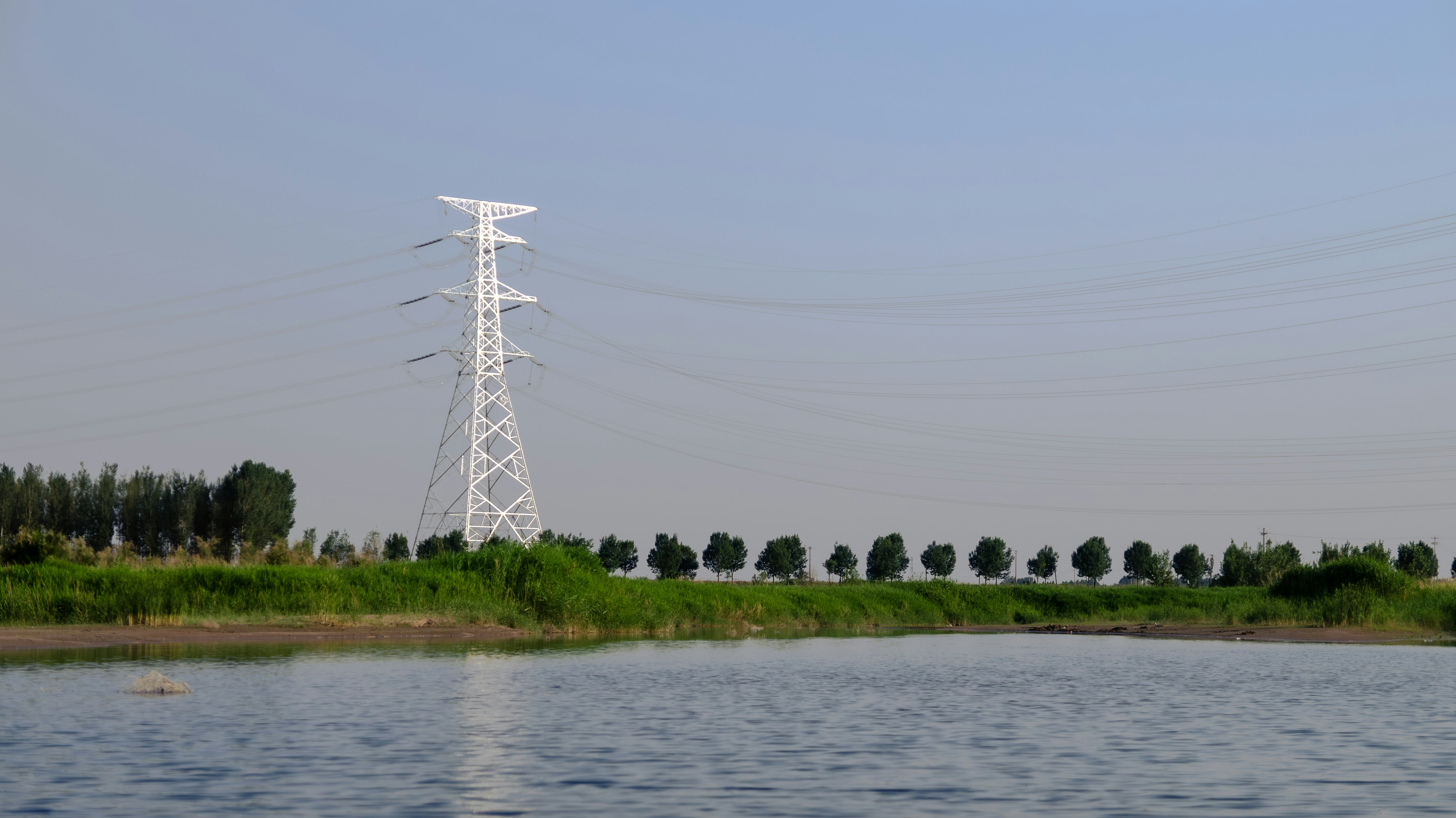 Power lines cross the lake under a blue sky.