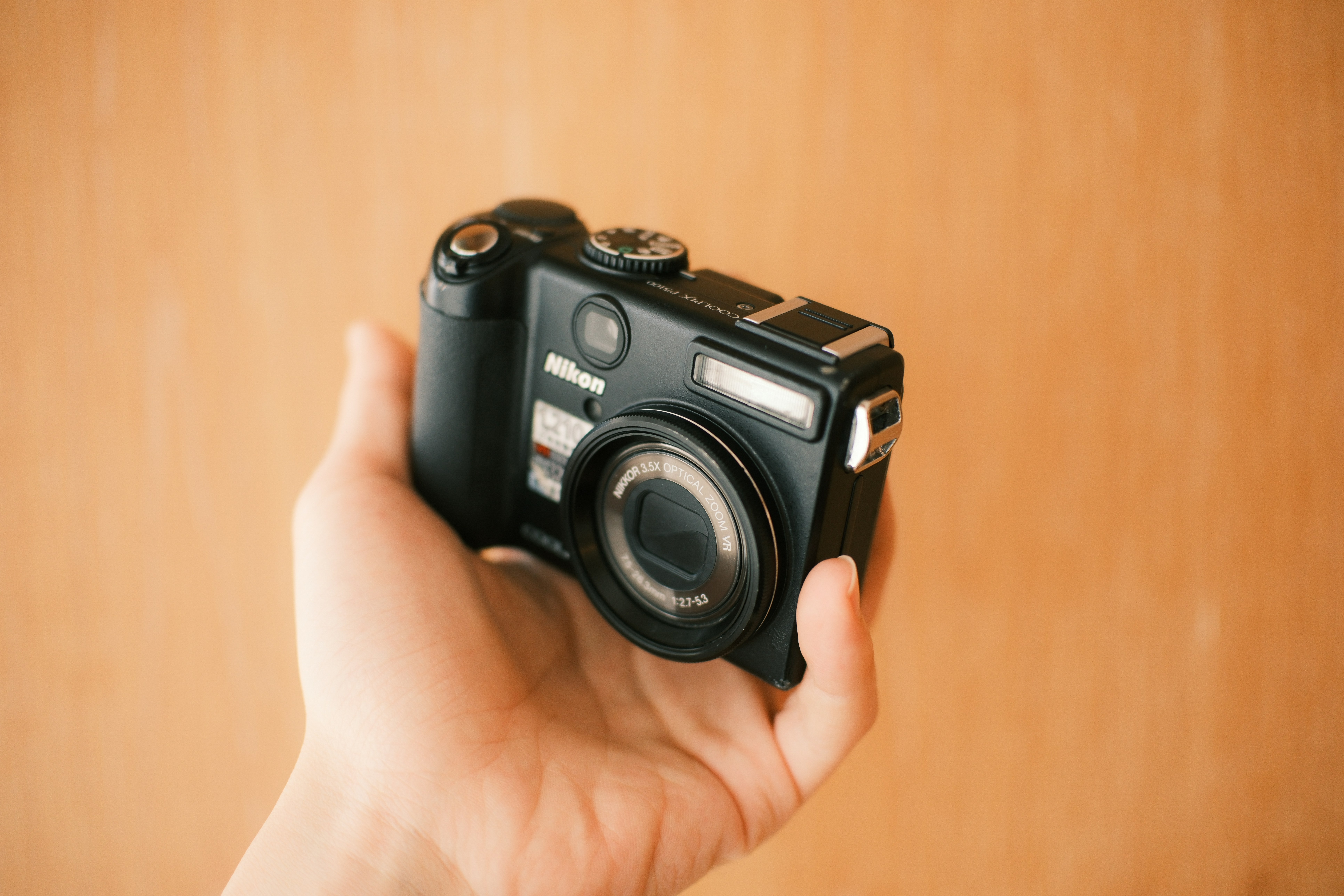 A hand holds a black digital camera.