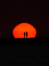 Two figures stand silhouetted against the sunset.