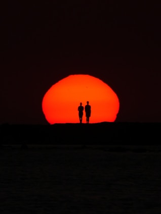 Two figures stand silhouetted against the sunset.