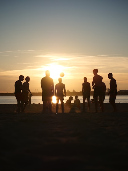 People play soccer on a beach at sunset.