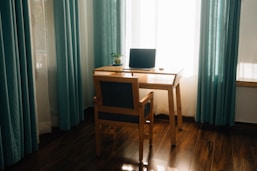 A desk, chair, and laptop in front of a window.
