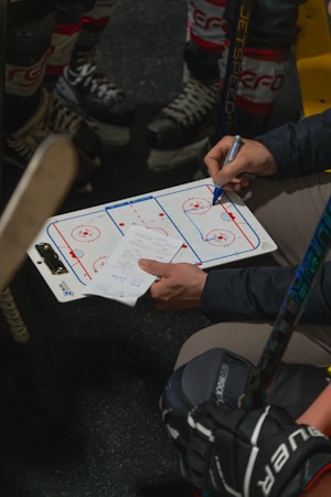 A hockey coach drawing plays on a whiteboard during a team huddle at the bench