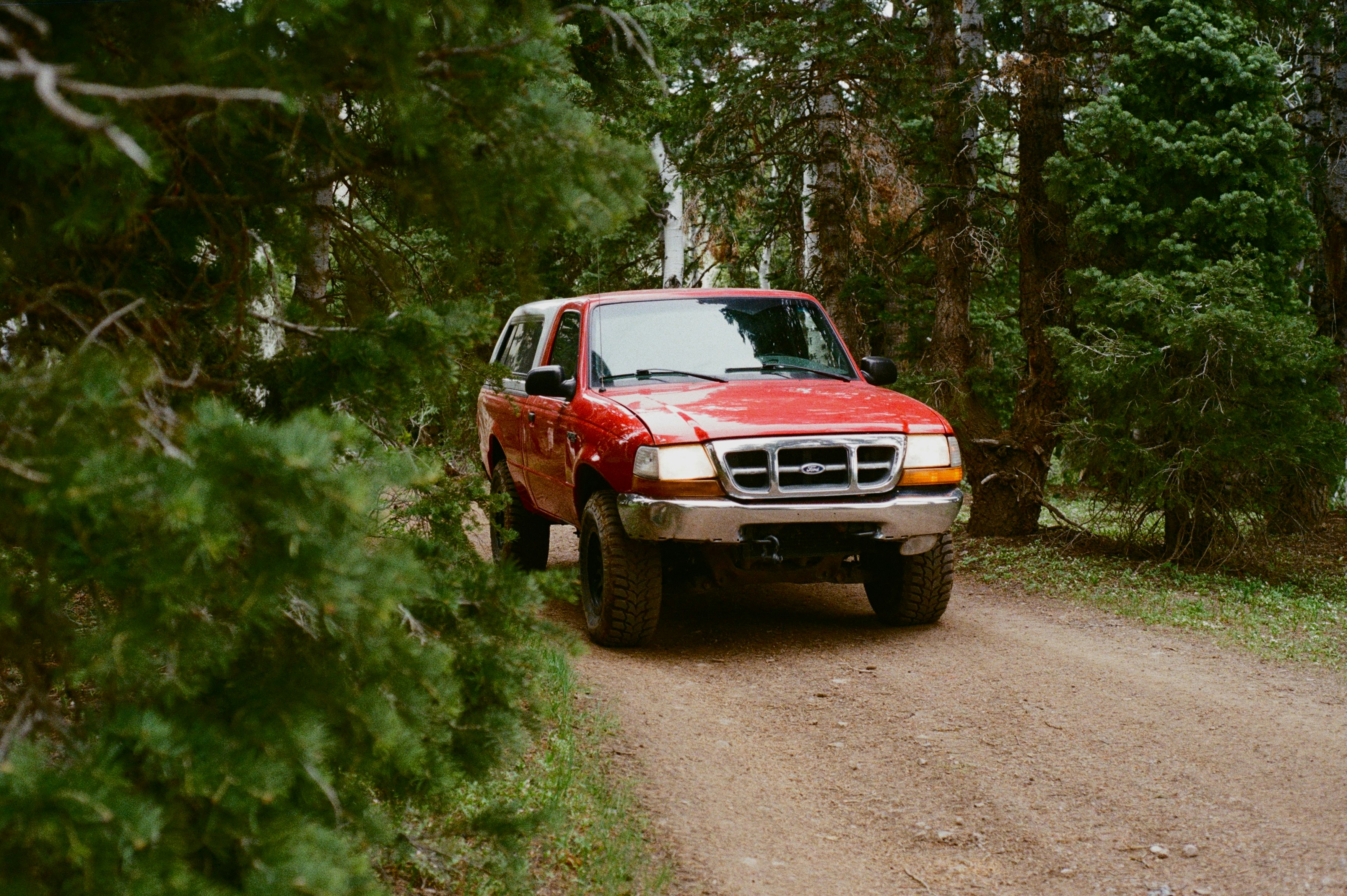 A red truck is driving on a dirt road.