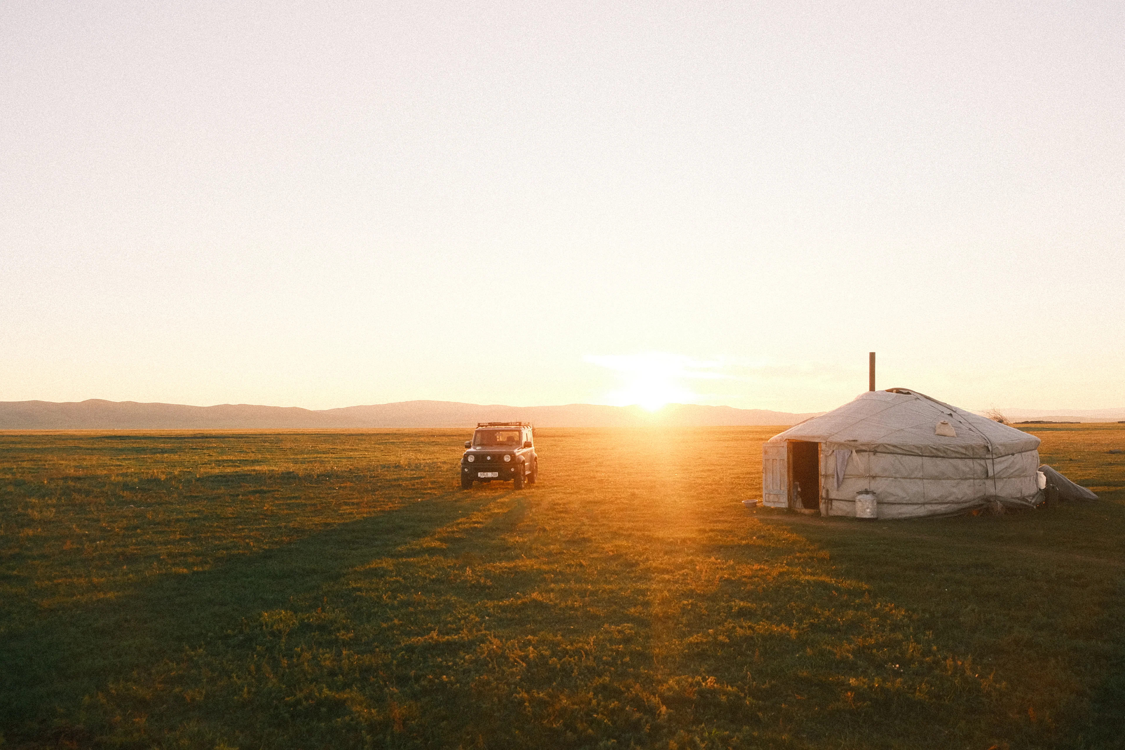 The sun setting behind a ger and a 4x4 on the open steppe