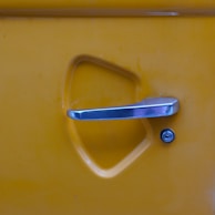 A shiny door handle and lock on a yellow car.