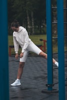 A woman stretches near a blue pole.