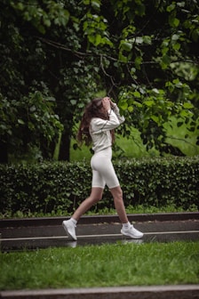 Woman jogs along a wet pathway near green trees.