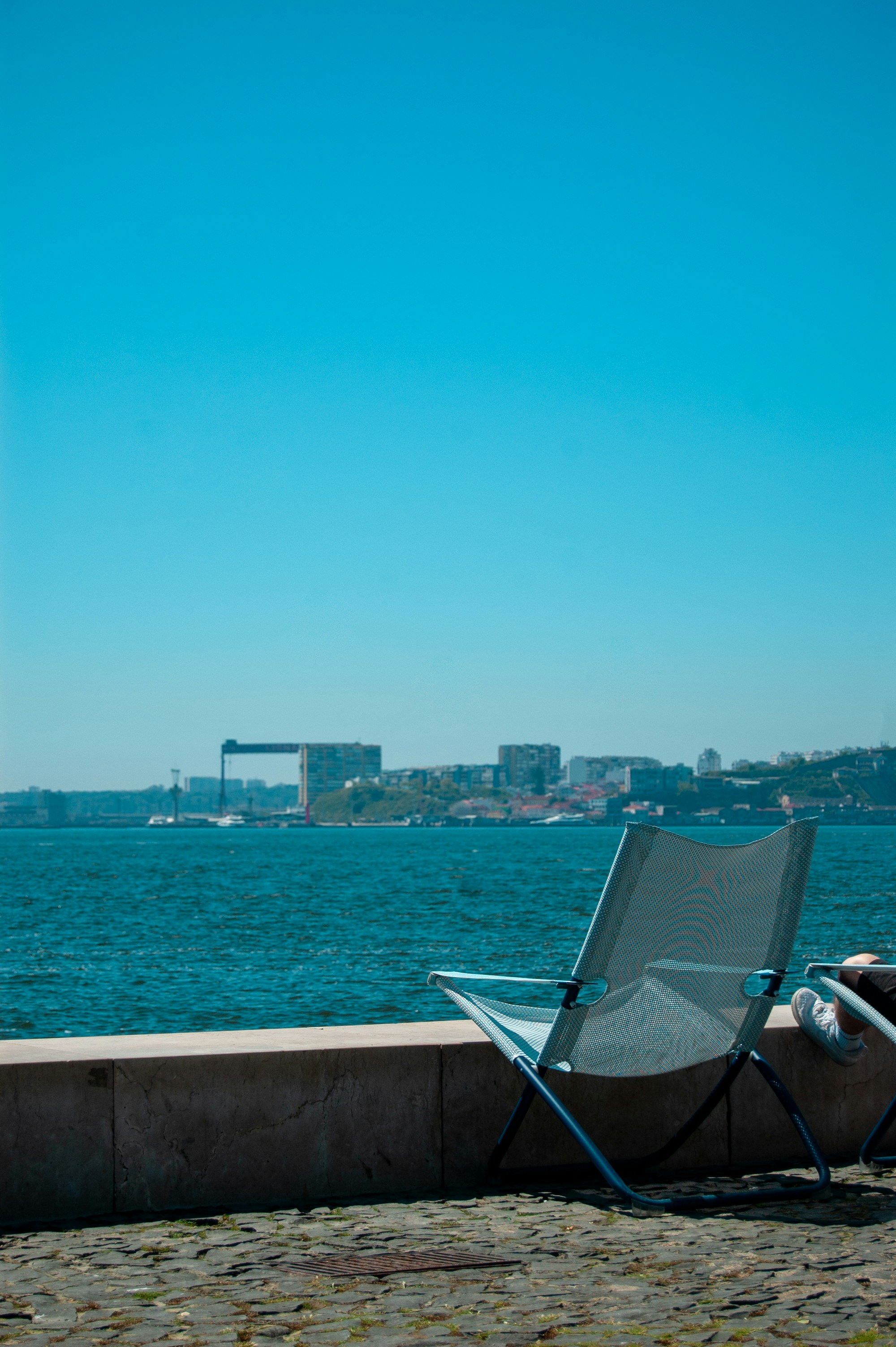 Chair overlooks the water with a city view.