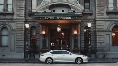 A lexus sedan parks in front of a hotel.