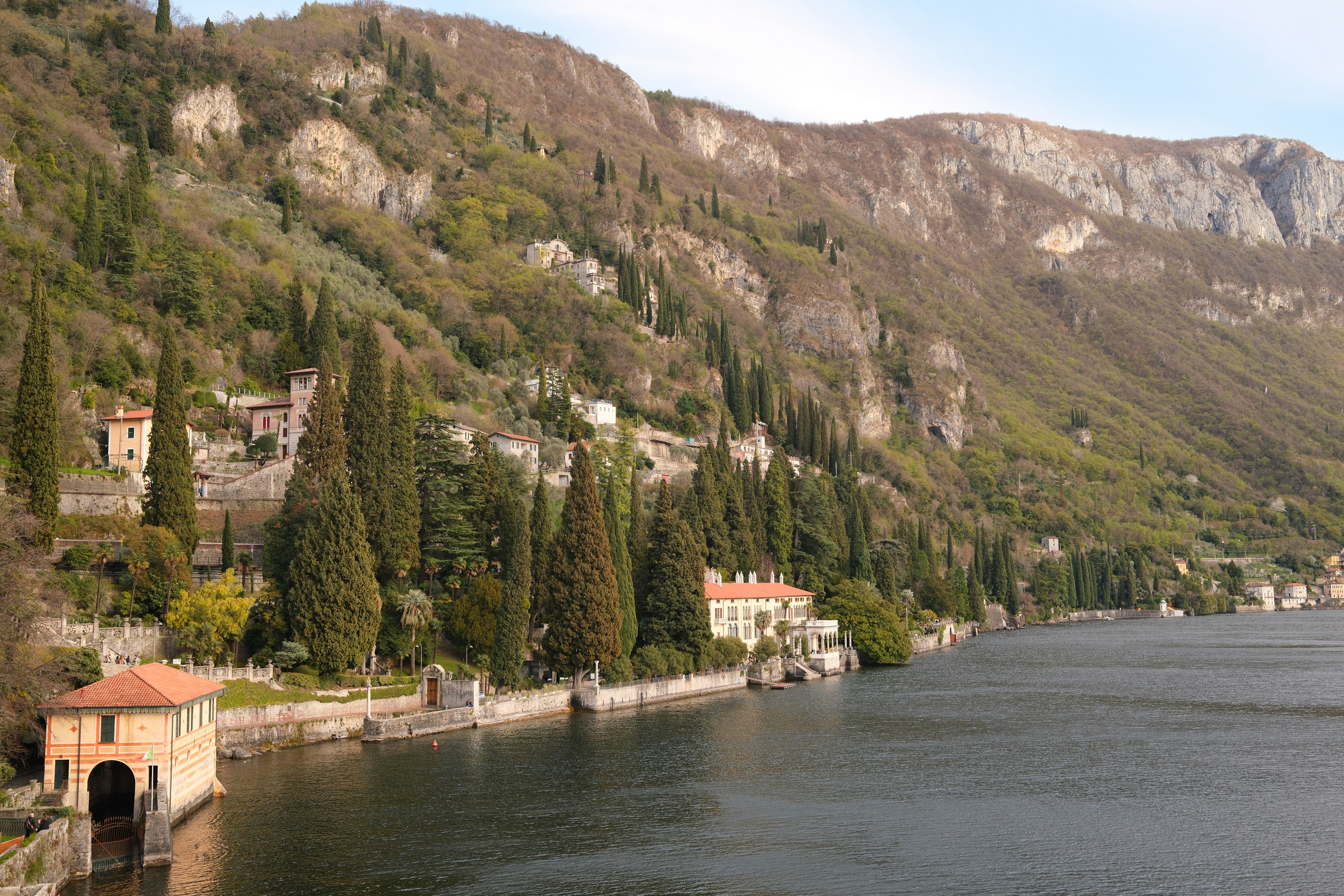 Lakeside buildings and mountains under a cloudy sky.