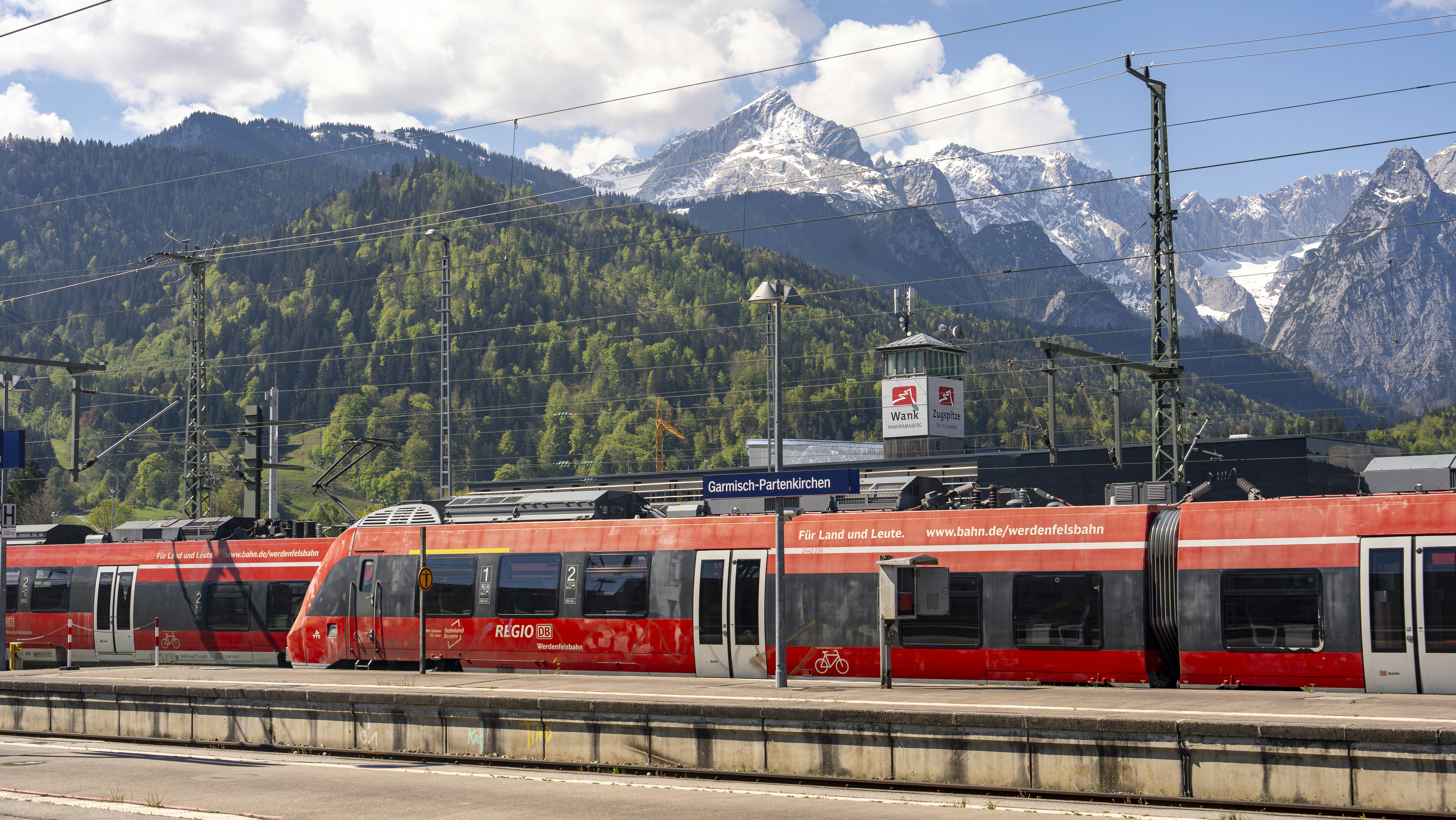 Red train at a station with mountains in the background.