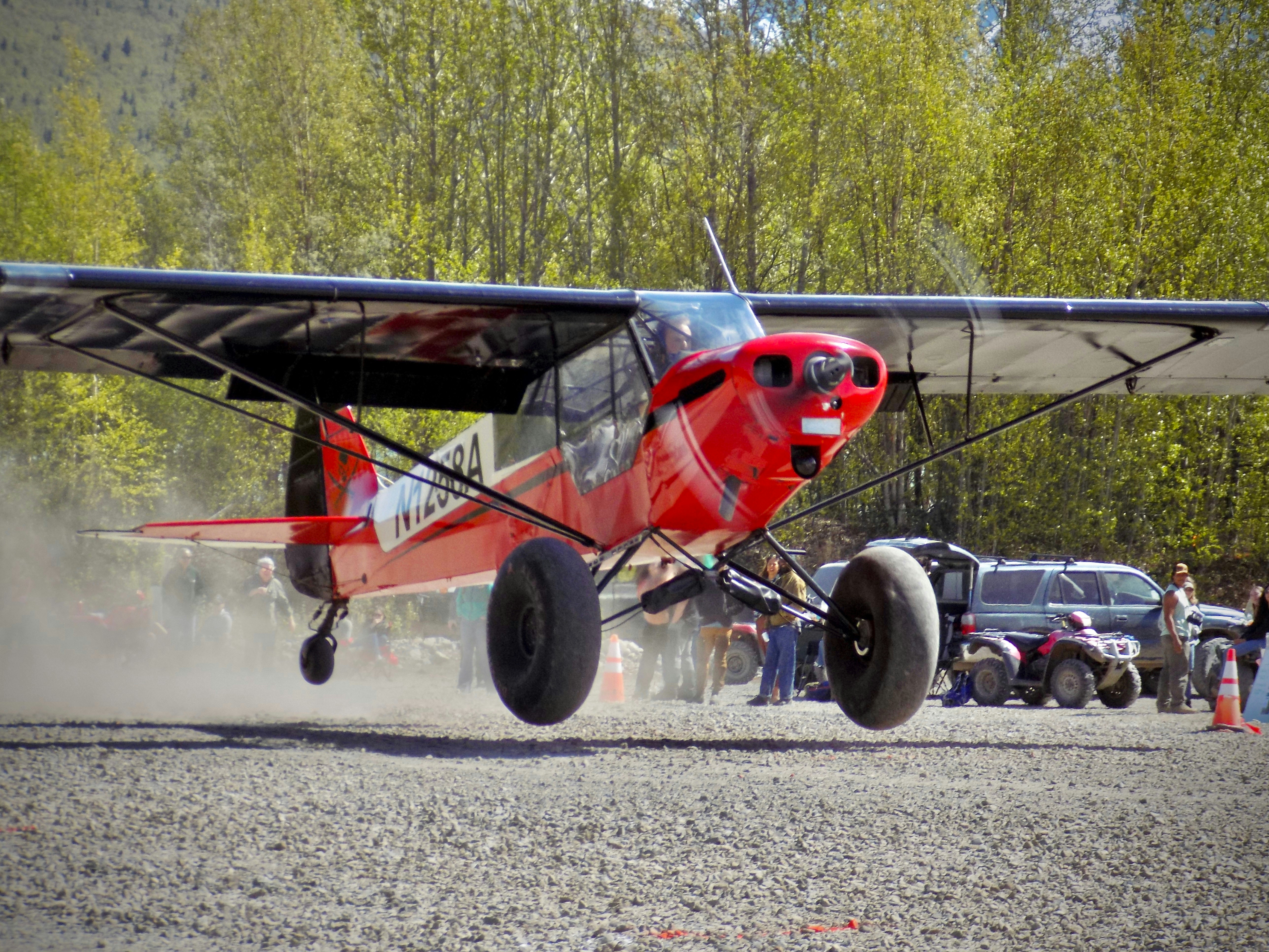 A red airplane is taking off from a gravel runway.