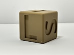 A tan cube toy with letter markings.