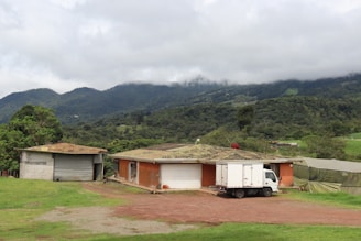 Rural buildings sit before a forested mountain.