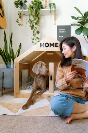 Woman reading next to dog in modern dog house.