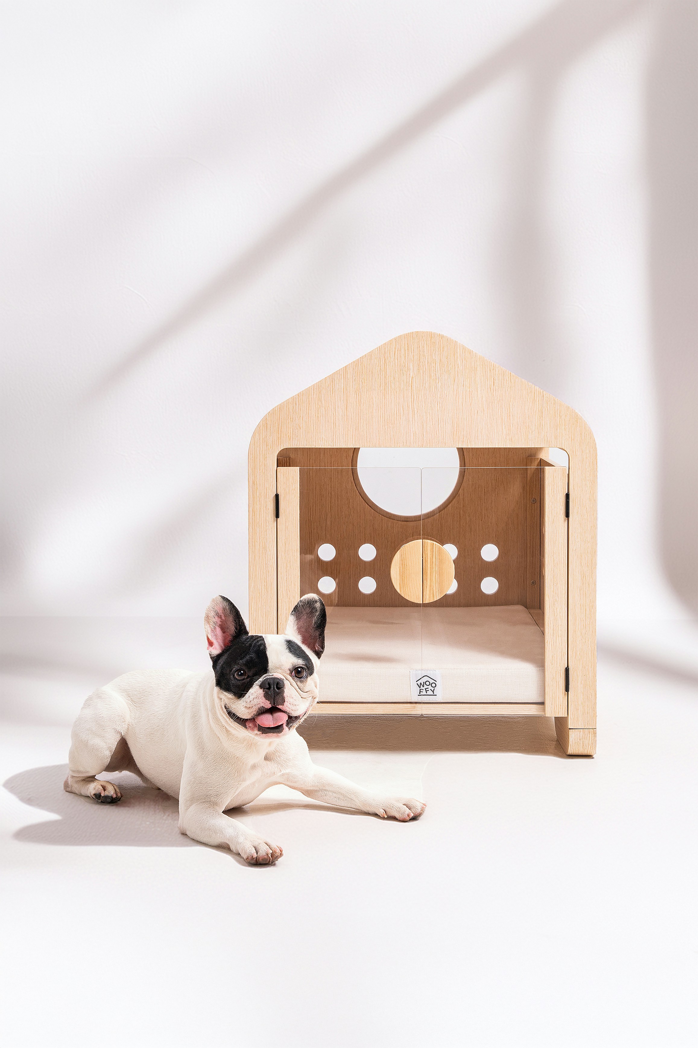 French bulldog lies next to a modern wooden dog house.