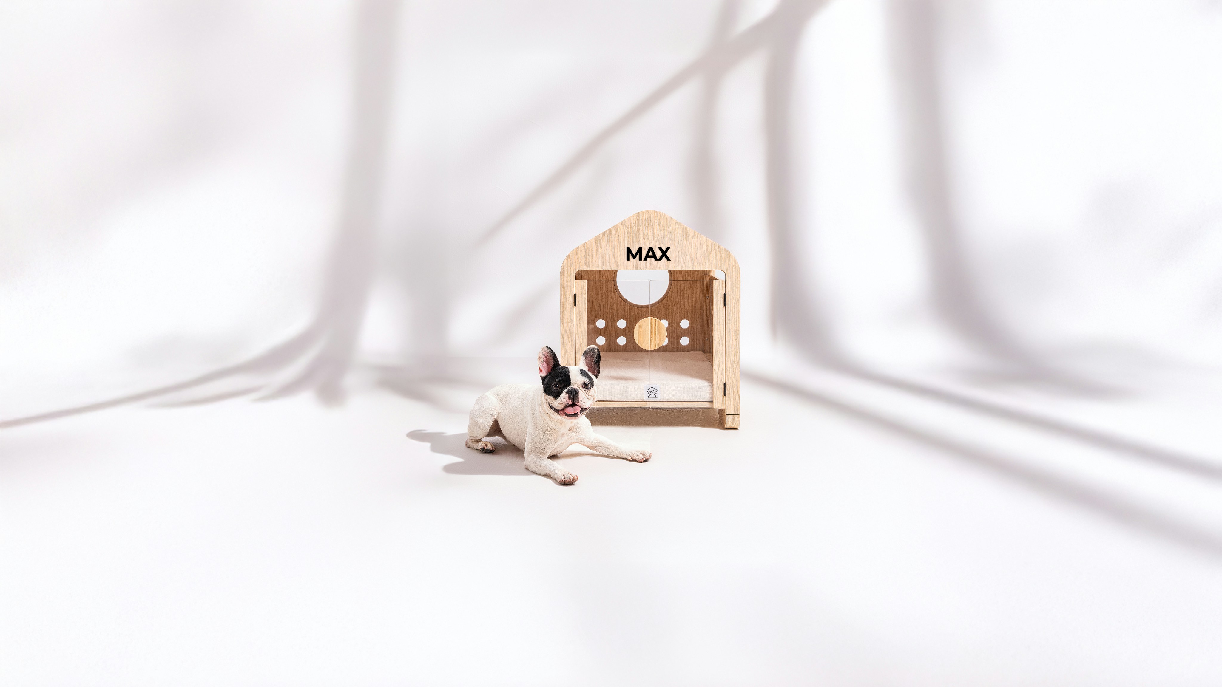 A small dog lies next to a wooden dog house.