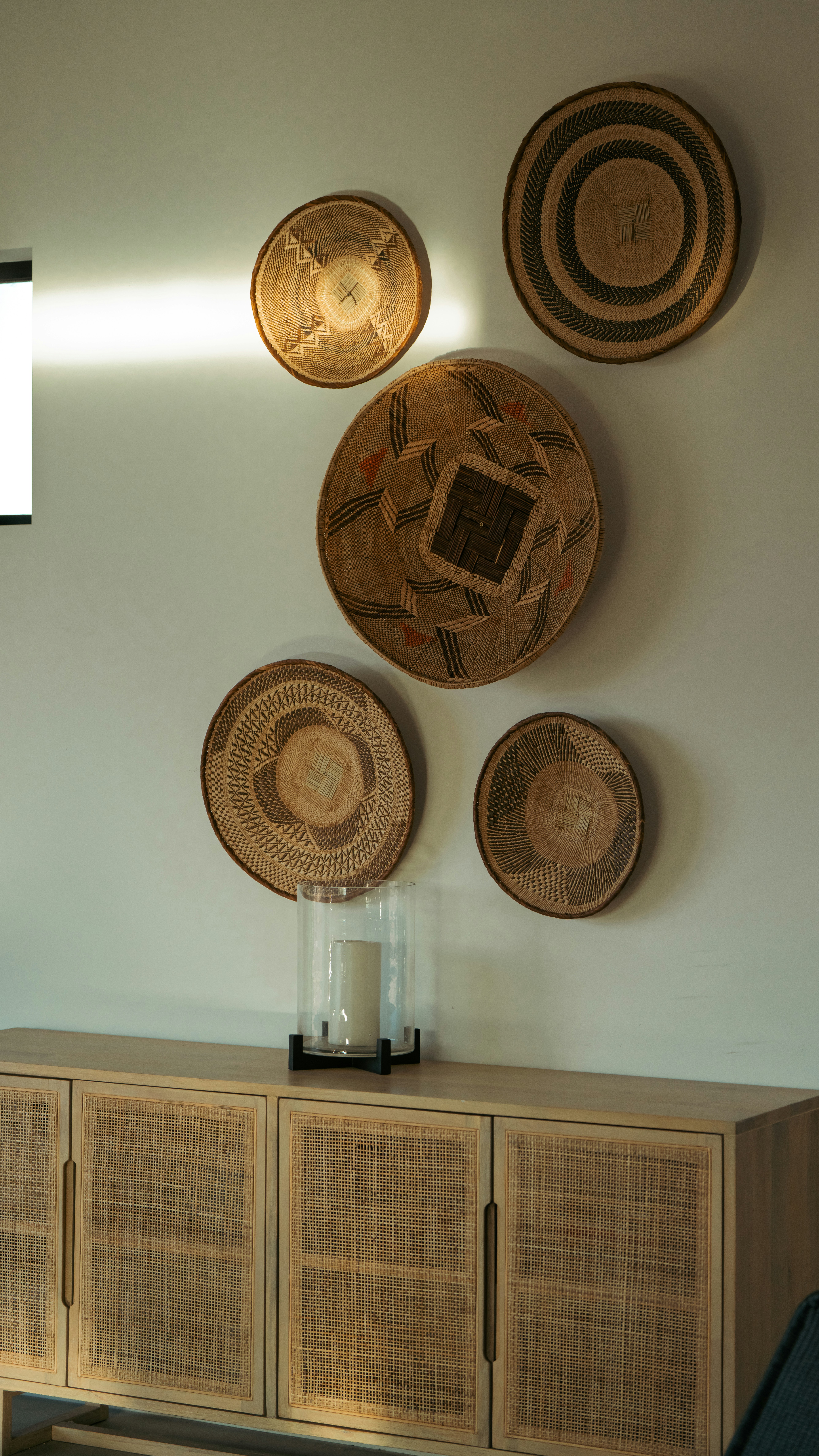 Woven baskets decorate a wall above a wooden sideboard.