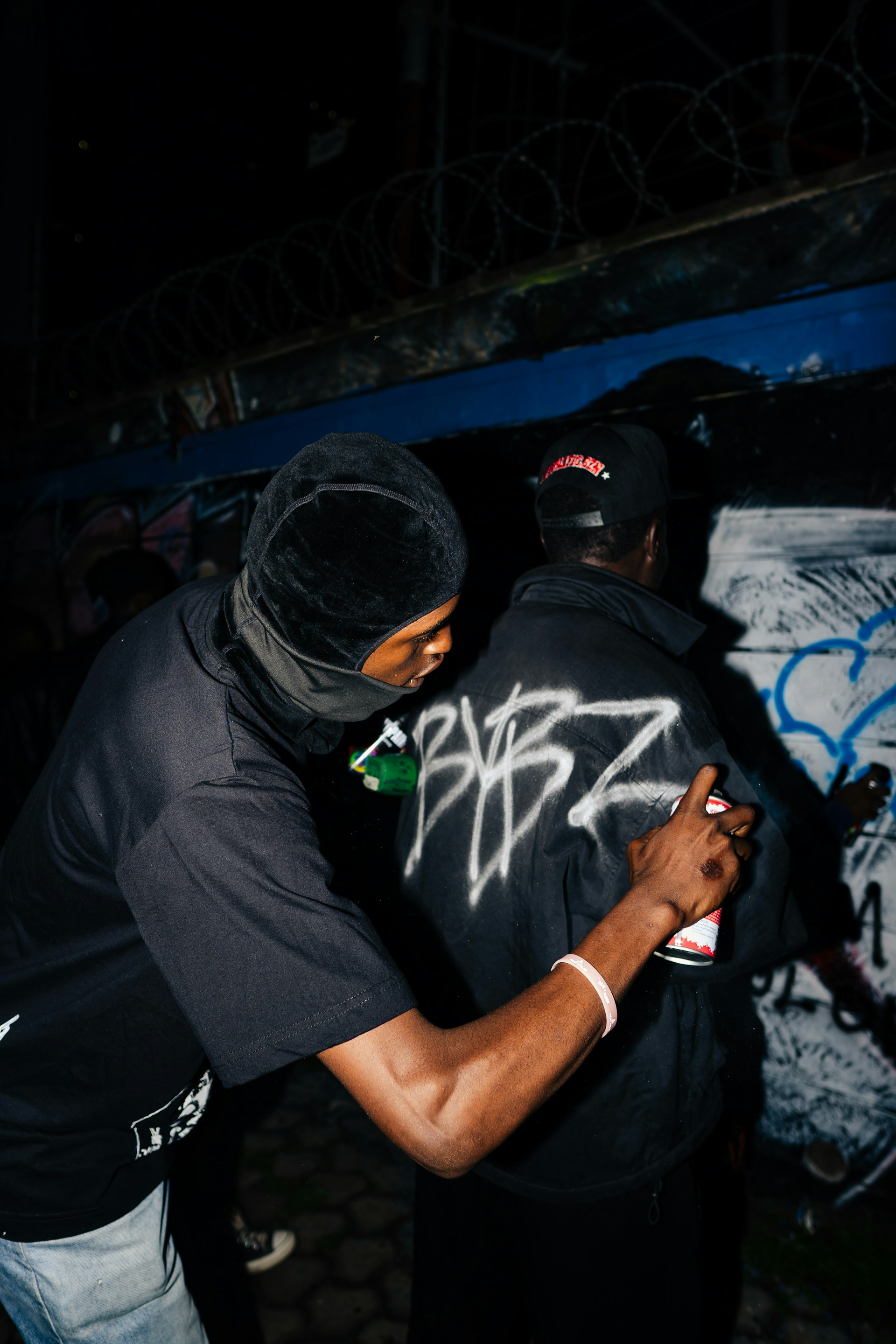 Two people graffiti tagging a wall at night.