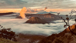 Volcanoes erupt amidst clouds at sunset.