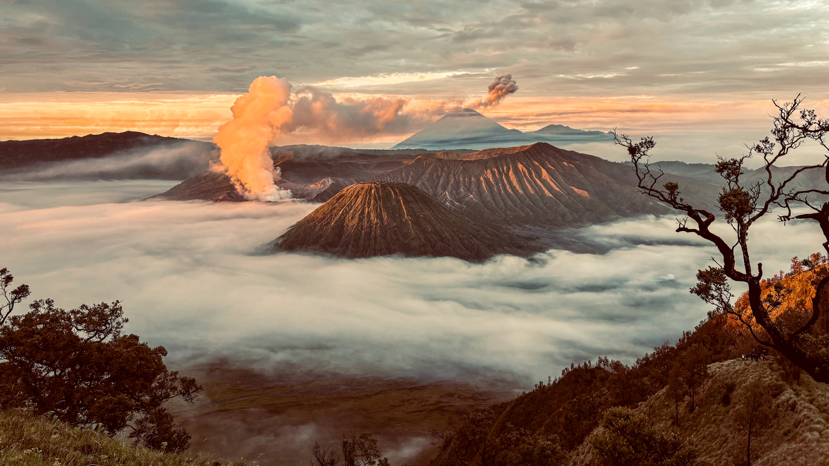 Mount Bromo and neighbouring volcanoes emerging through clouds at sunrise