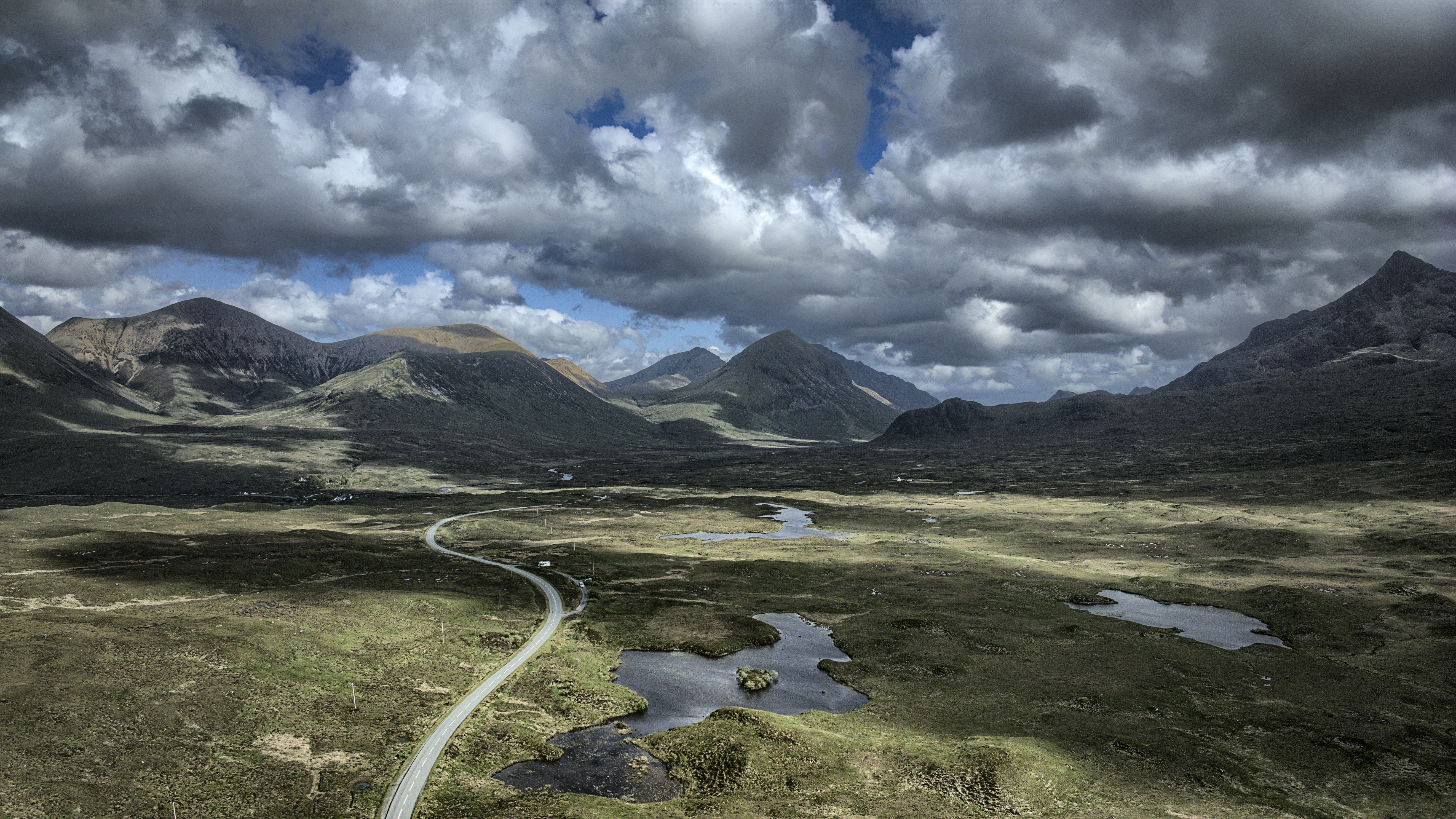 Mountains and winding road under a dramatic sky.