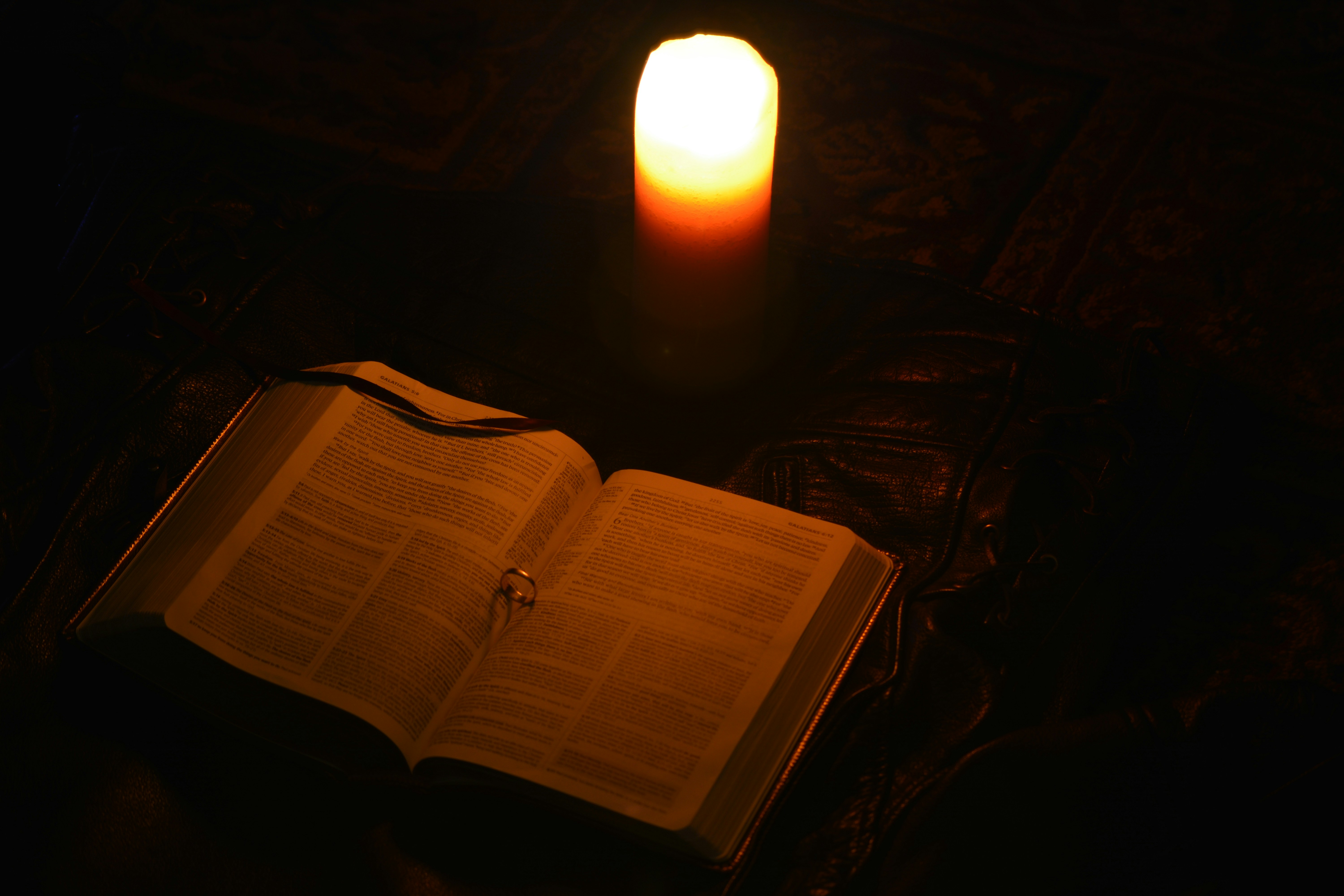 A lit candle illuminates an open book.