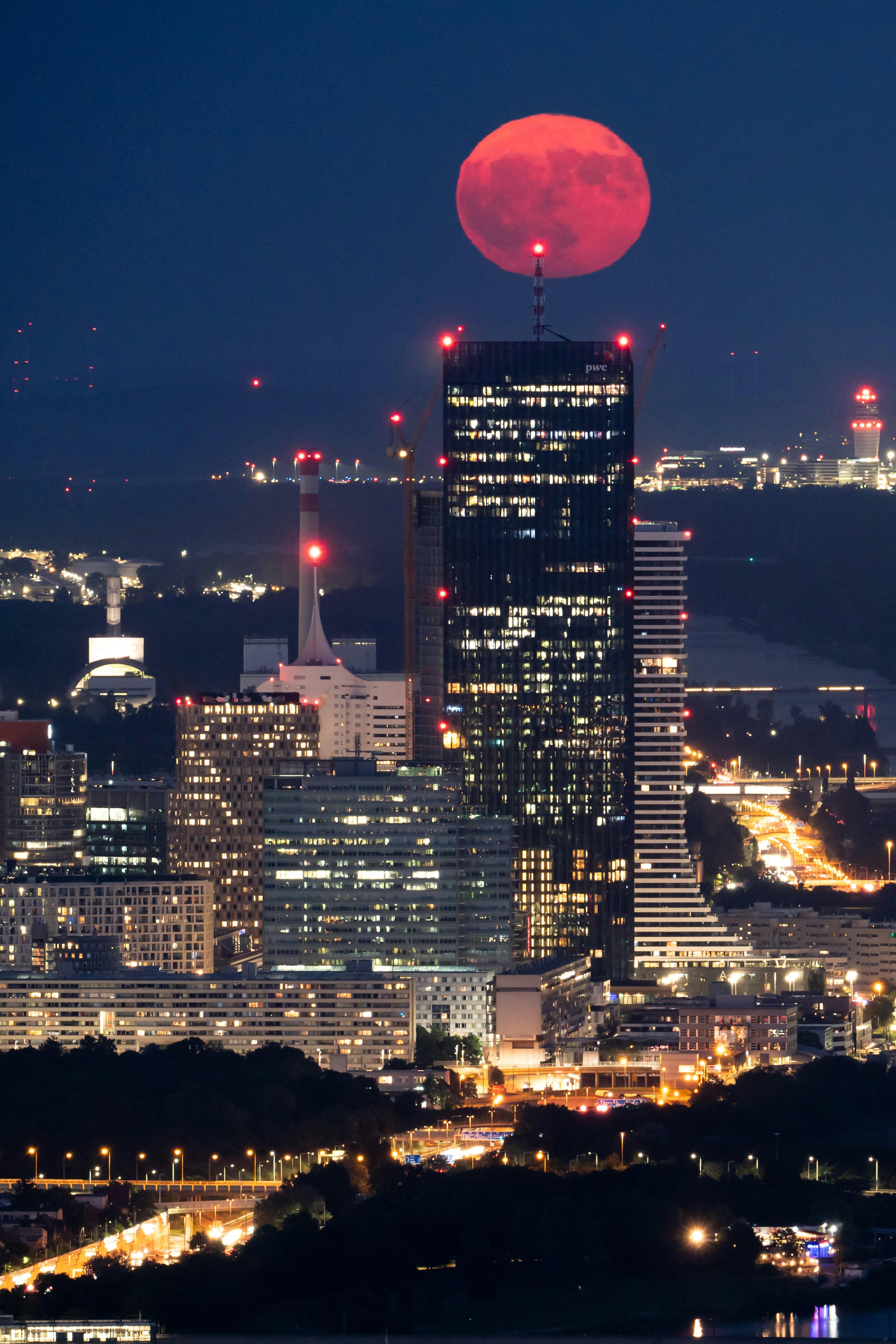 Red moon rising above a brightly lit cityscape.