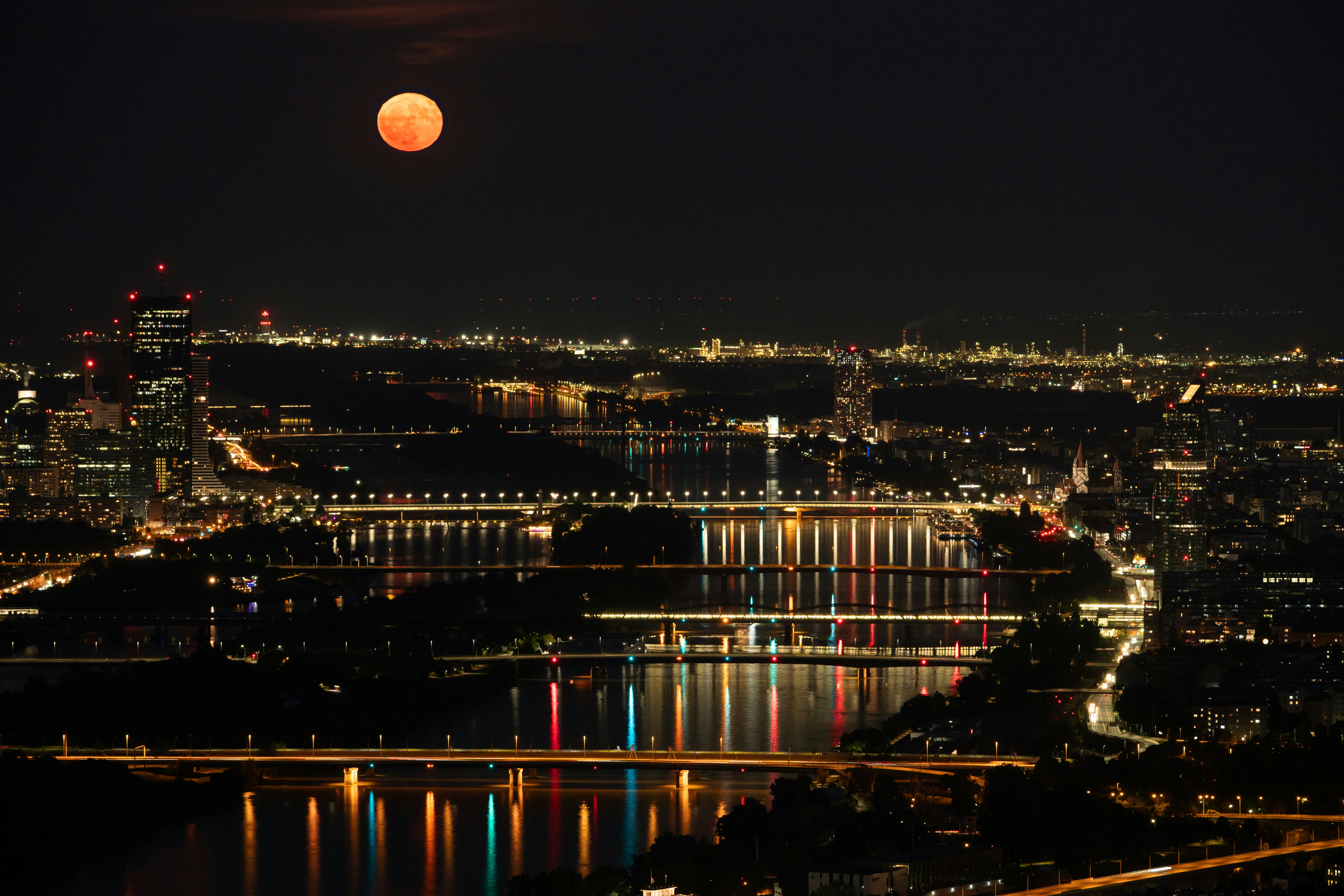 A red moon rises over a city at night.
