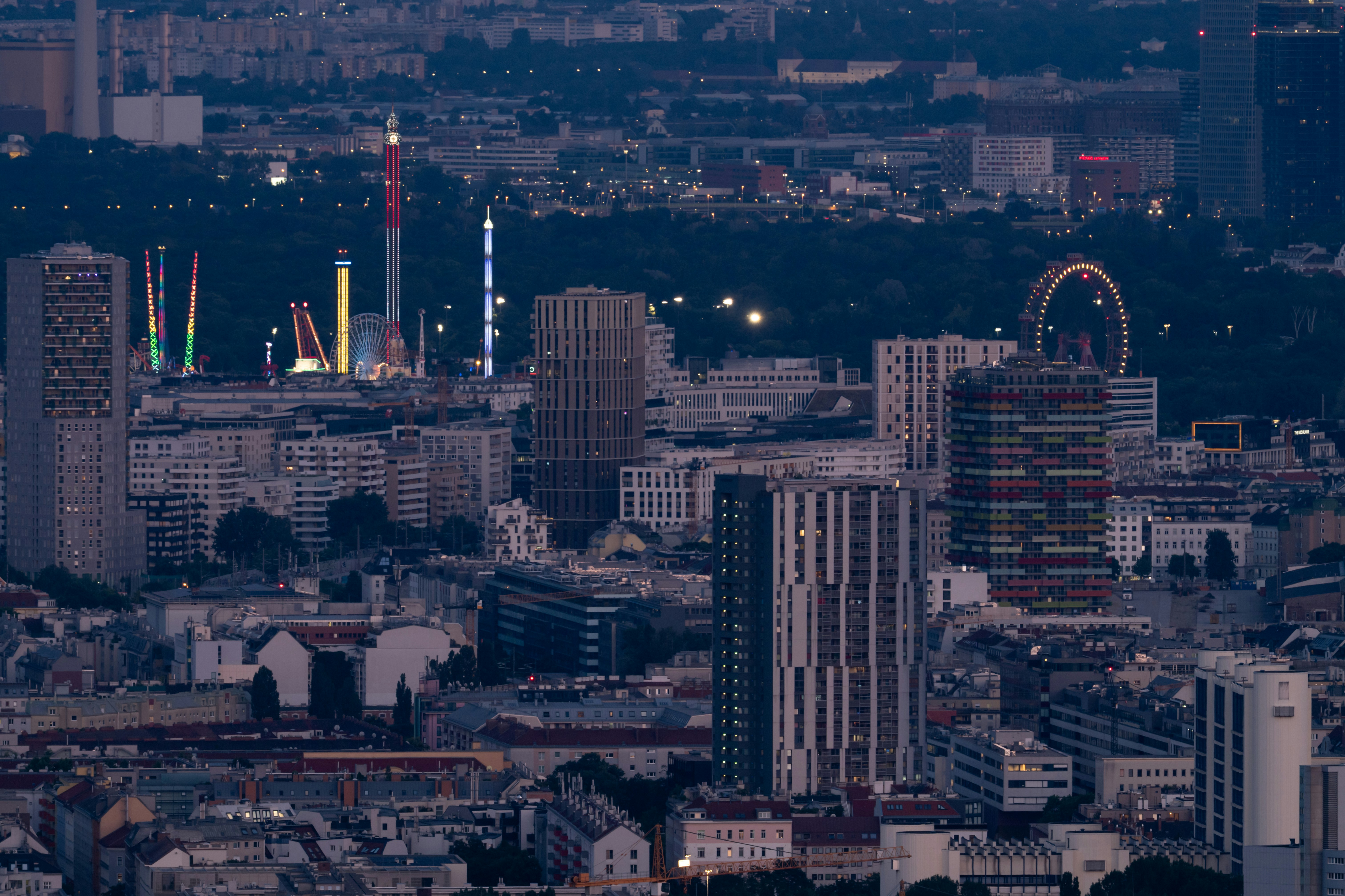 Cityscape at dusk with amusement park in the distance.
