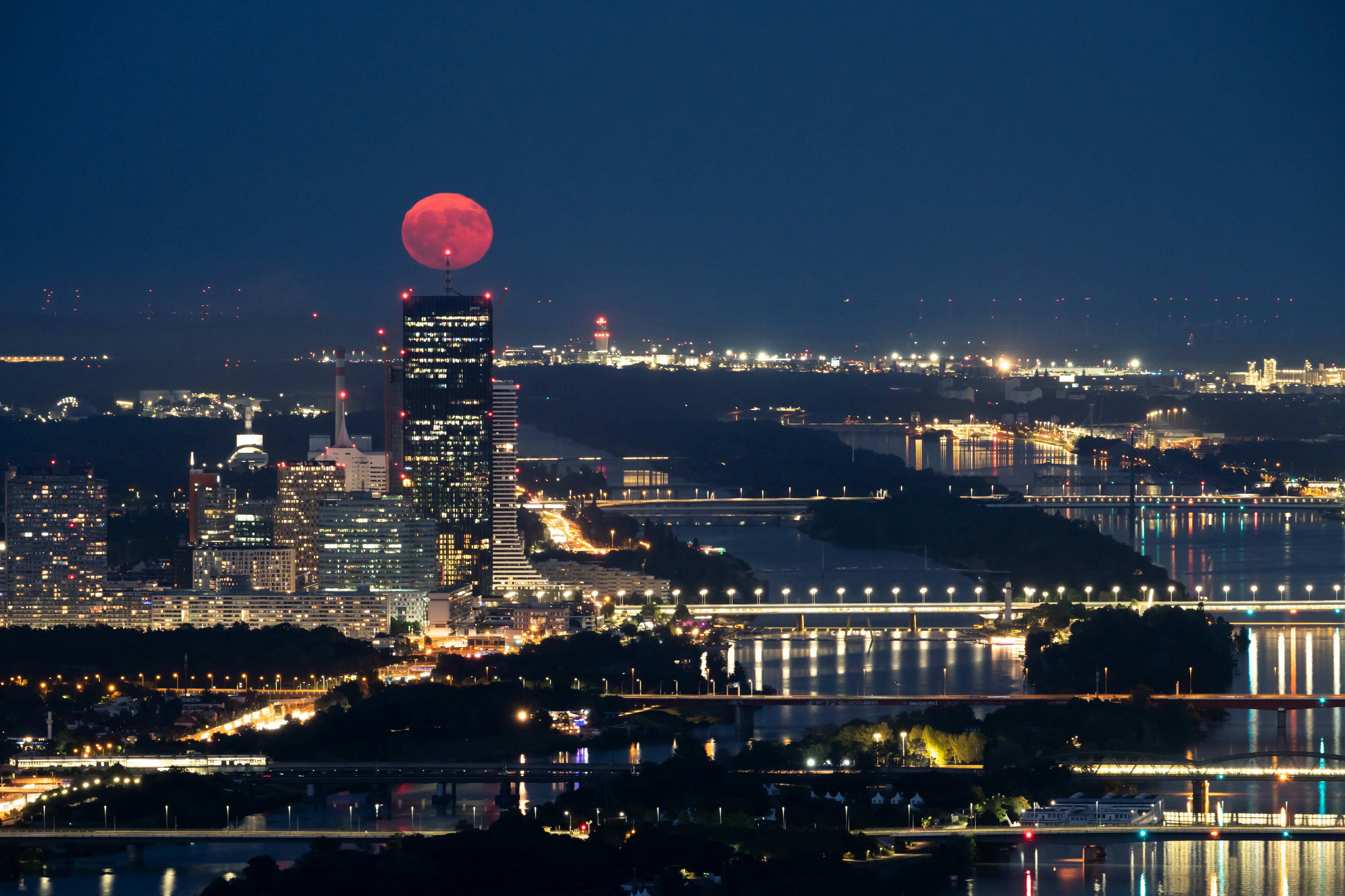 A red moon rises over a city at night.