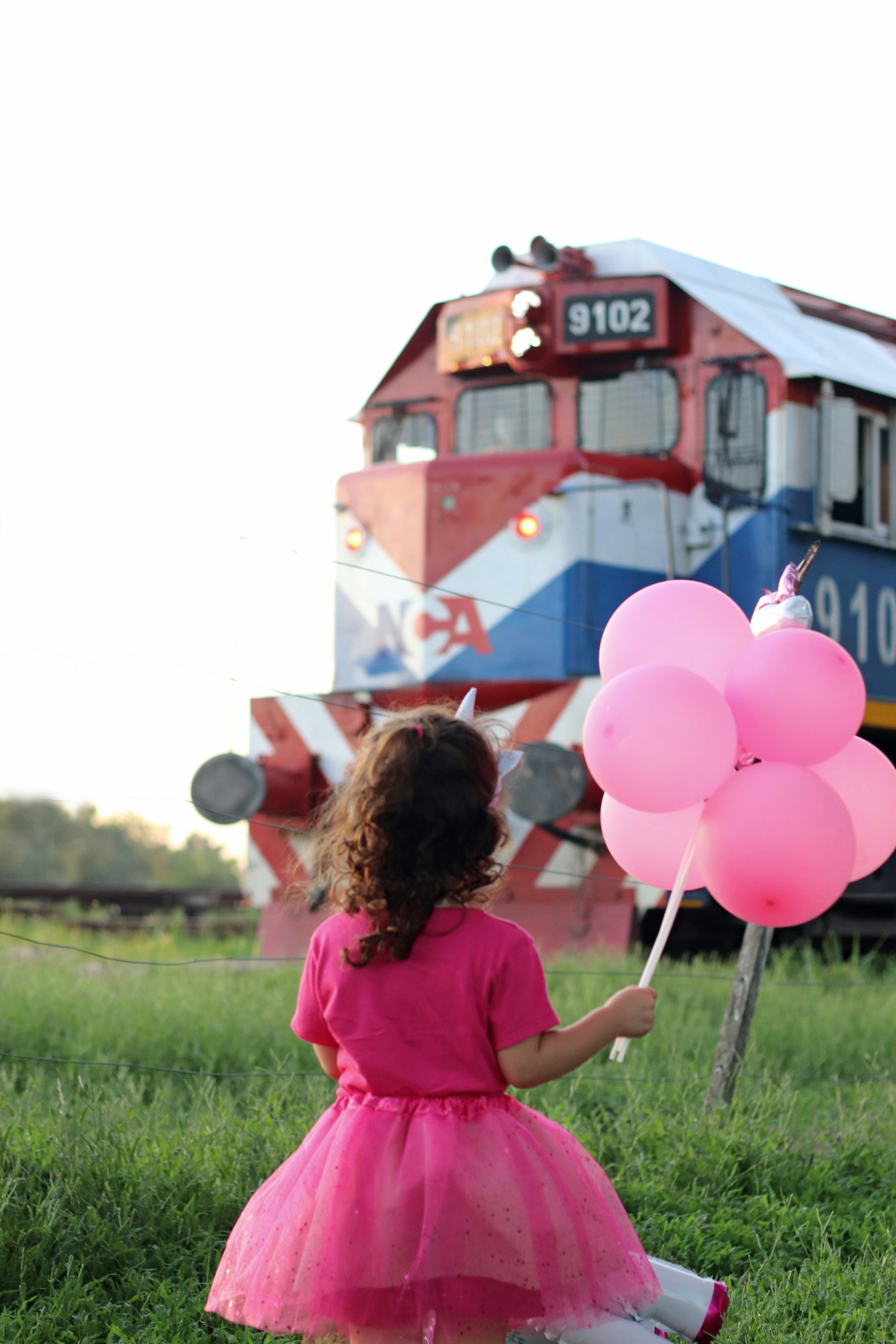 Girl in pink dress gazes at a train.