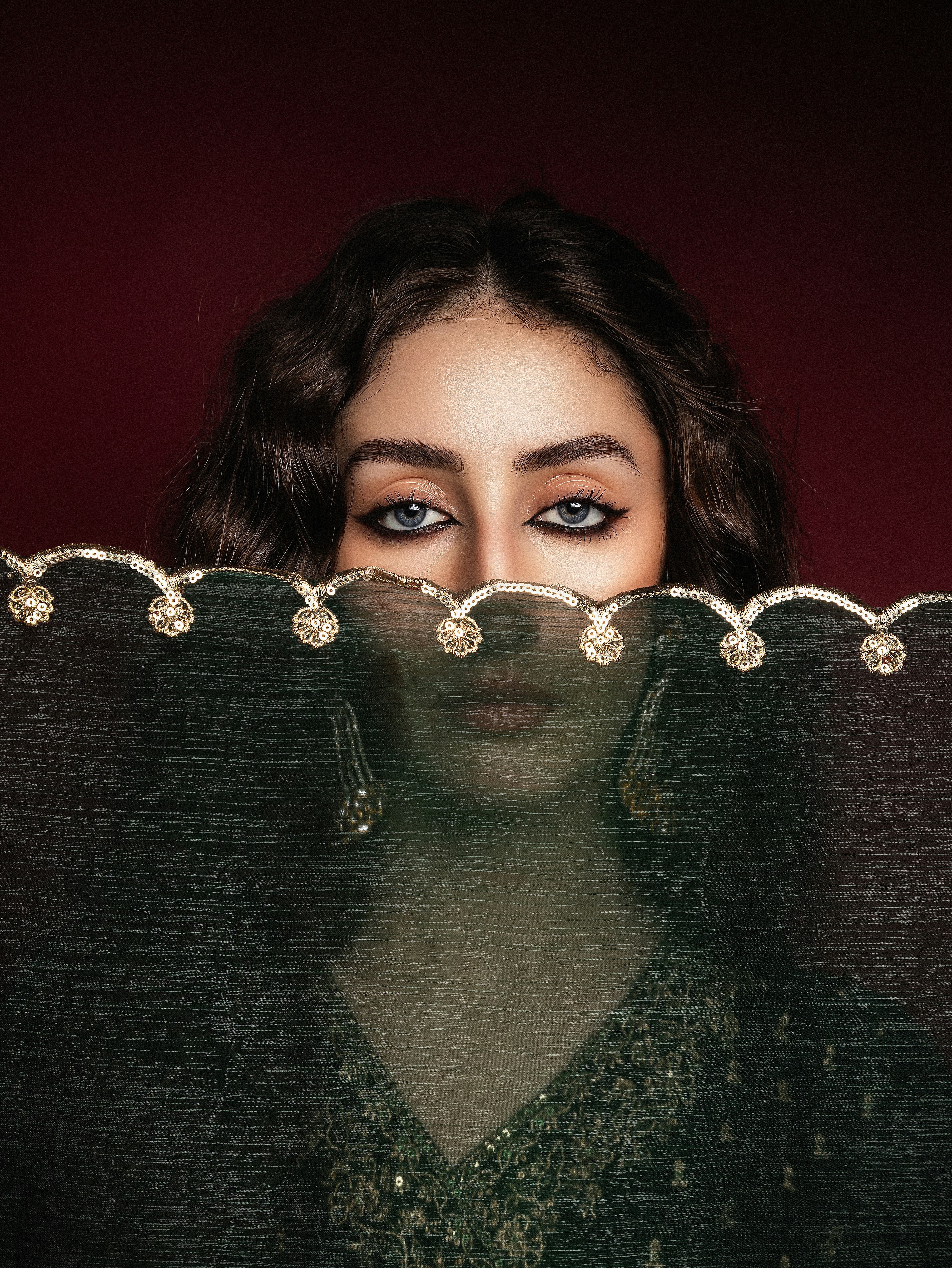 Eine Frau lugt hinter einem dekorativen Schleier hervor.