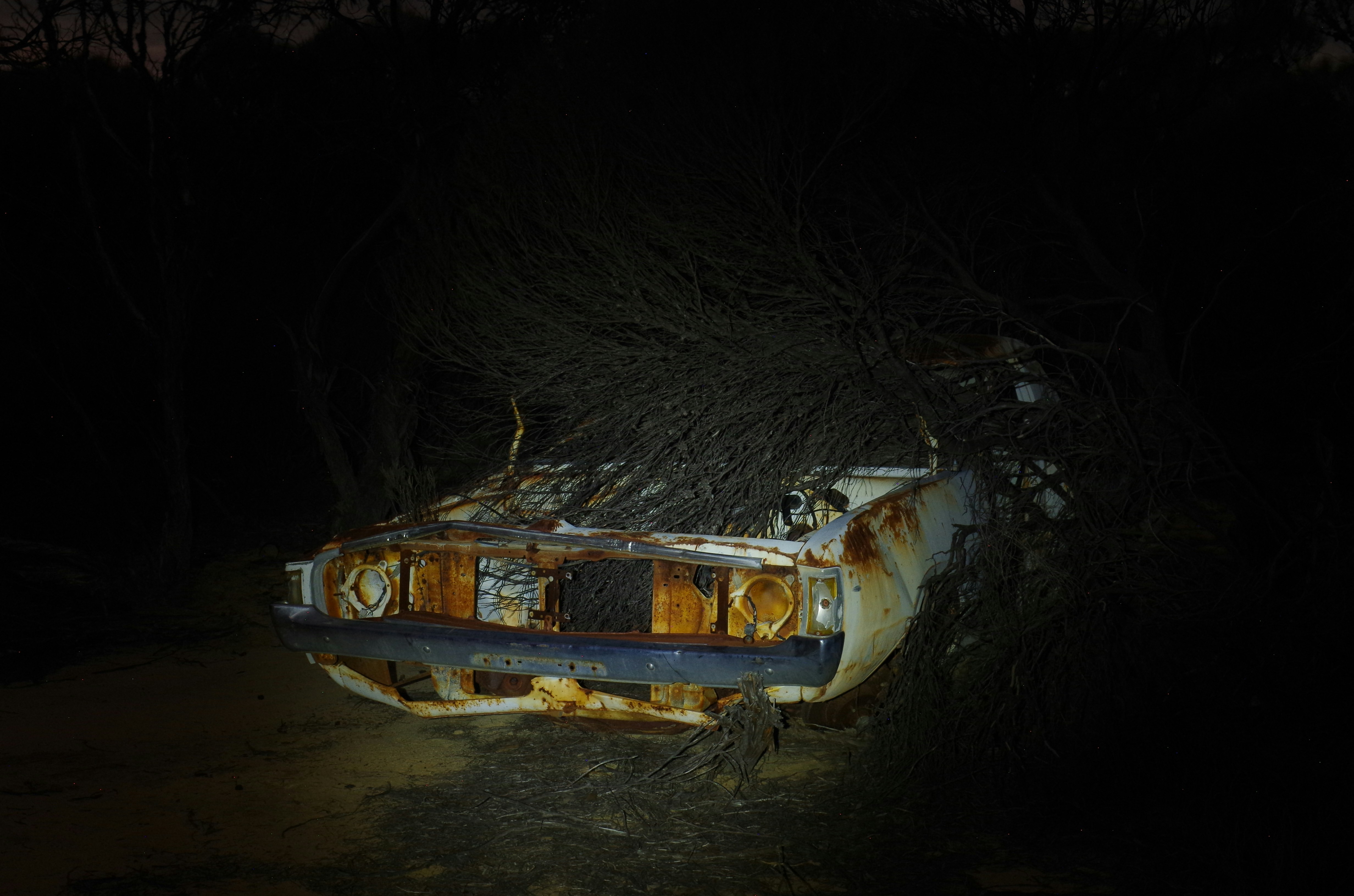 A rusted, abandoned car sits in the darkness.