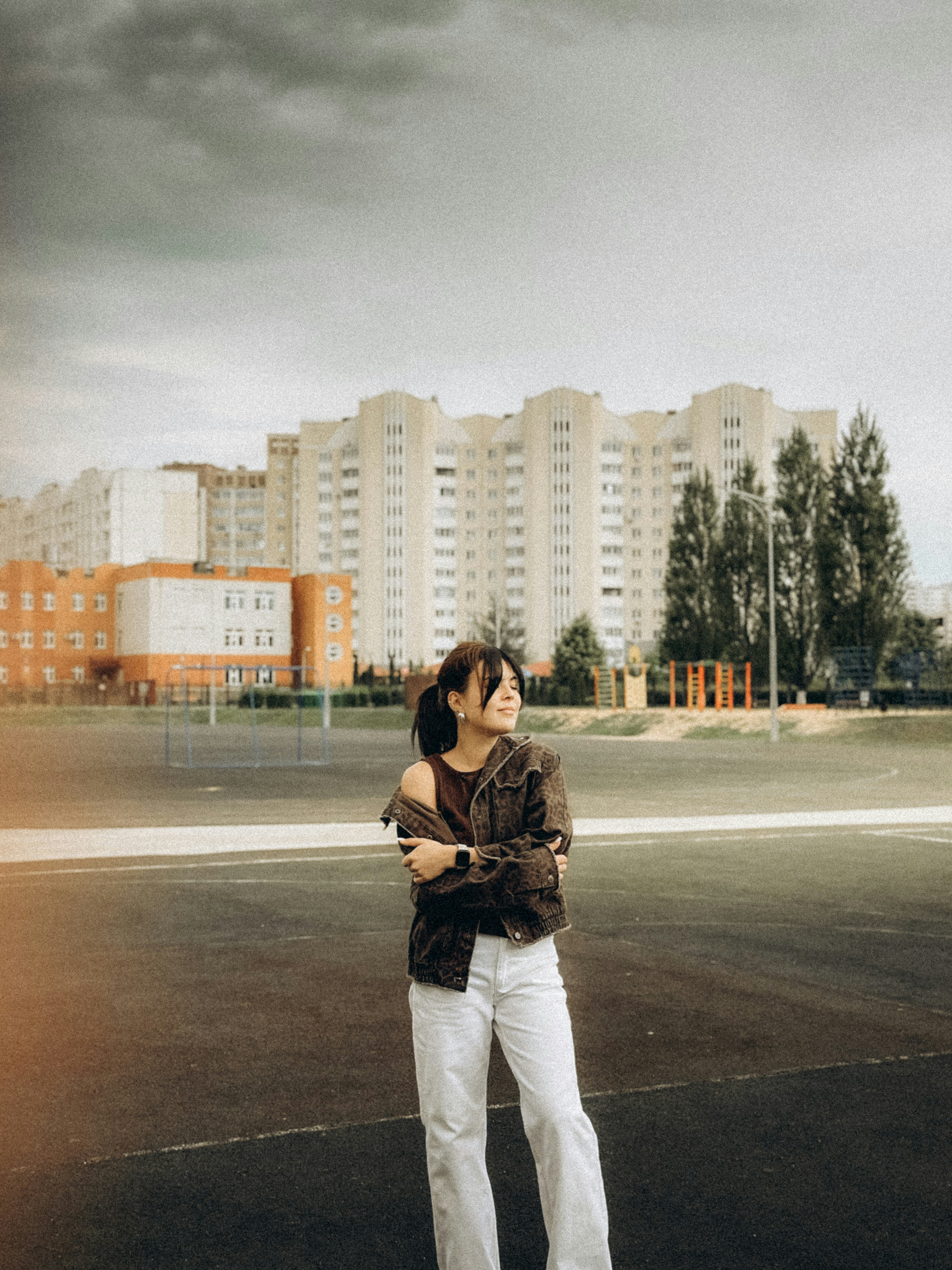 A woman poses outdoors with a building behind her.