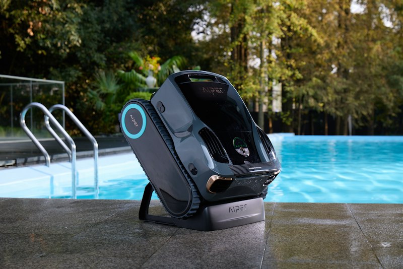 A robotic pool cleaner standing on a pool deck beside a swimming pool