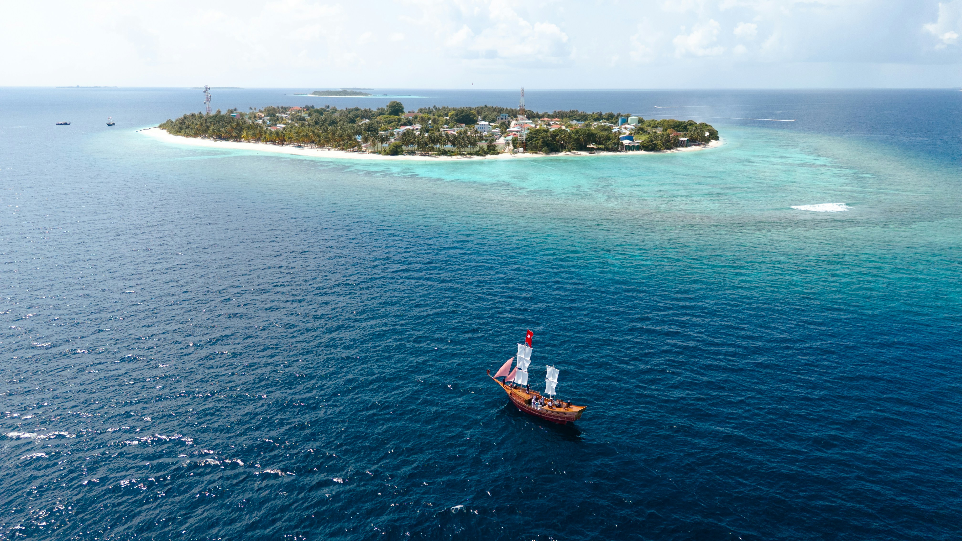 A traditional wooden sailboat with white sails on deep blue water near a tropical island