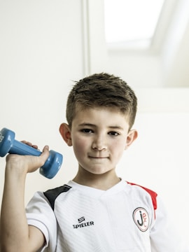 Boy is lifting a dumbbell and looking at the camera.