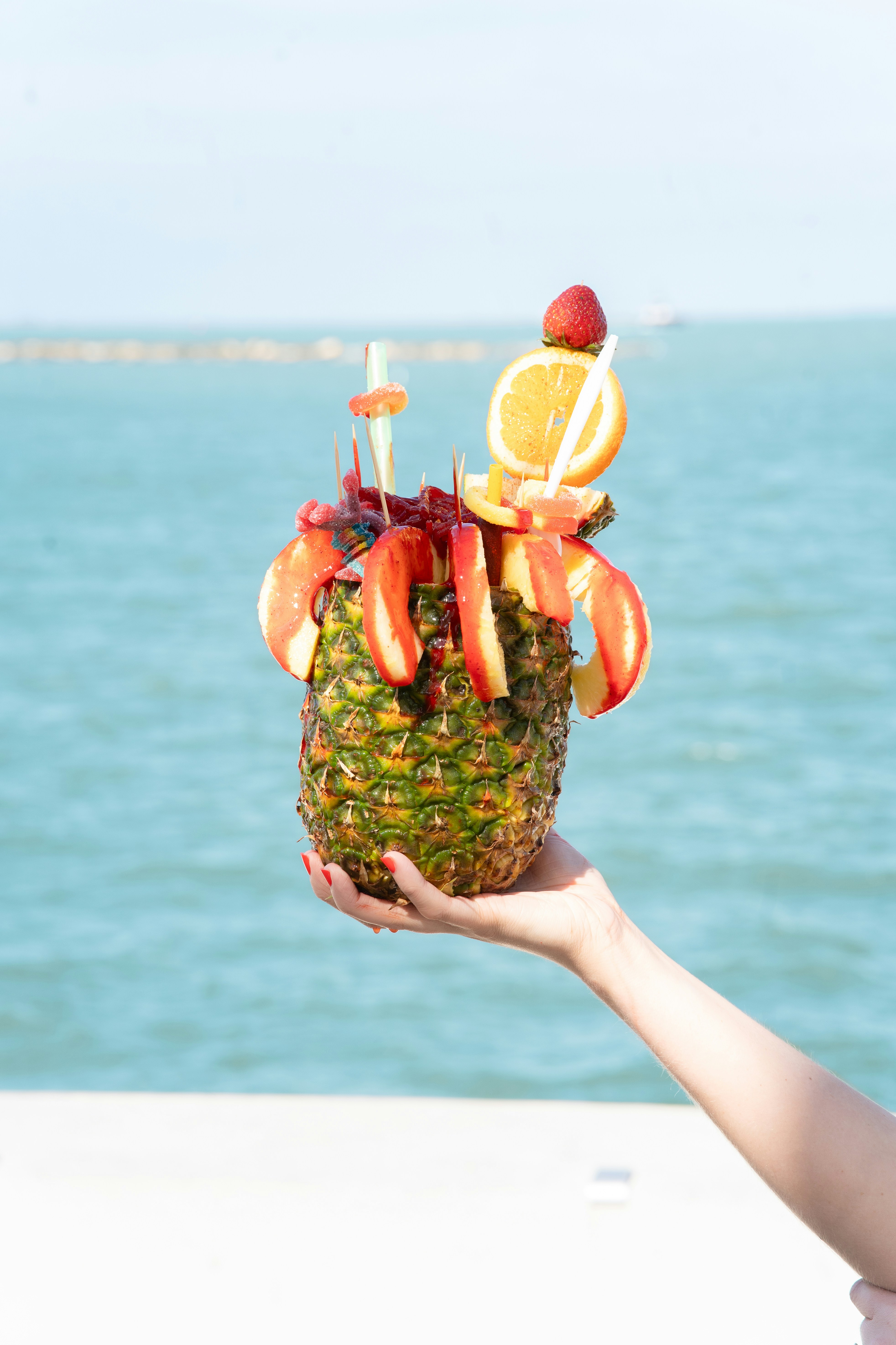 Hand holds a pineapple drink decorated with fruit.