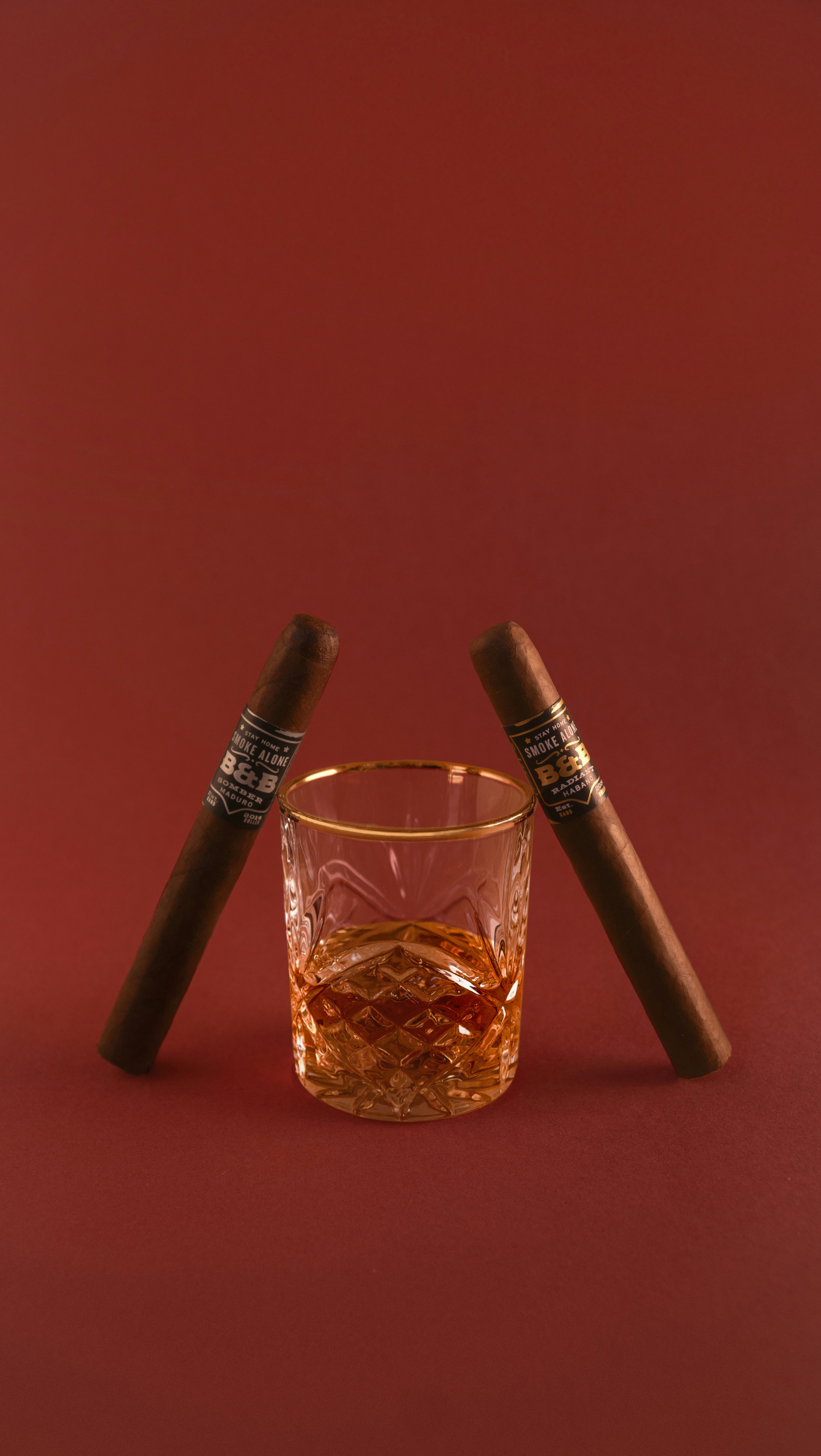 Cigars and whiskey sit on a red background.