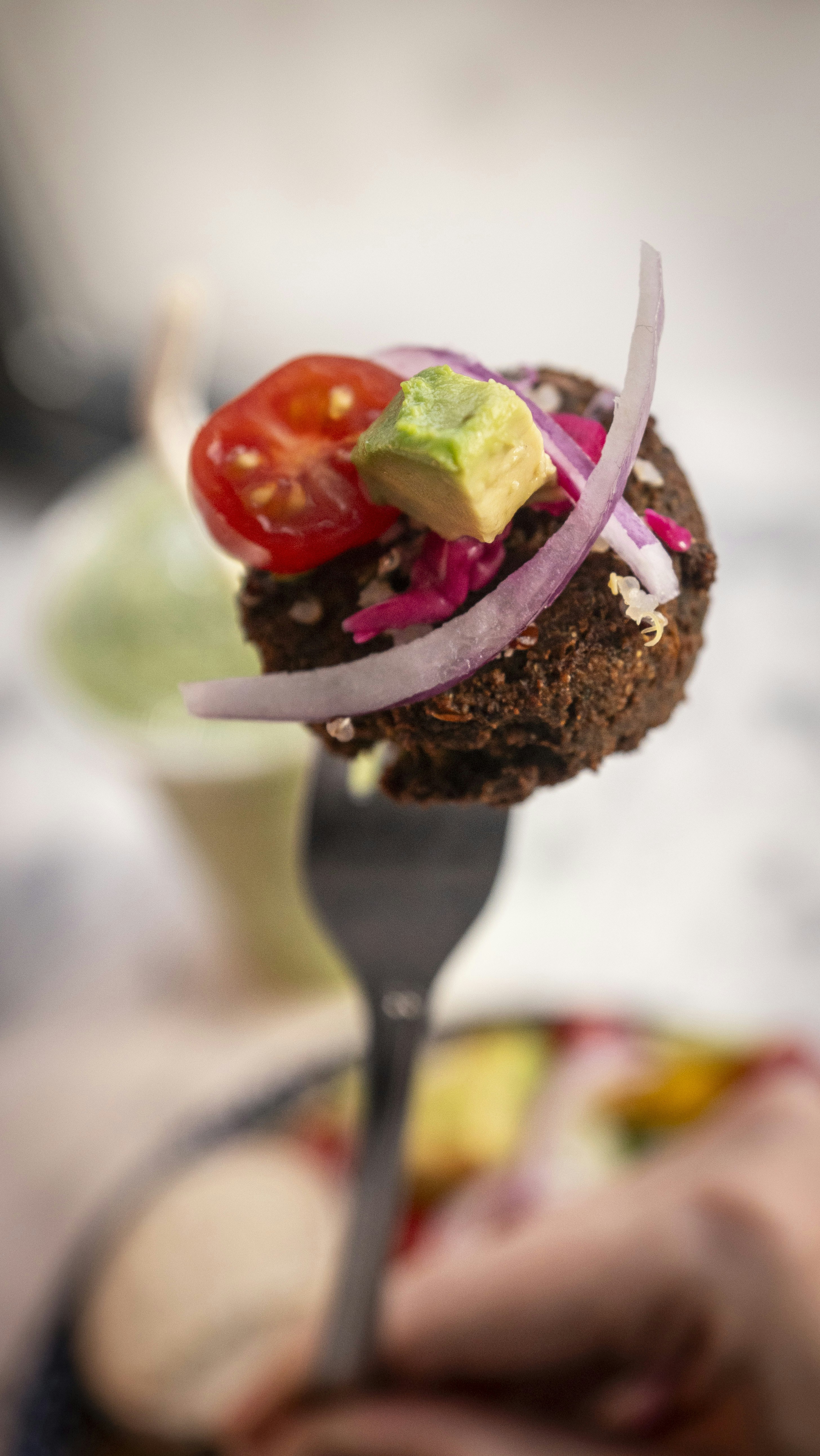 A falafel bite with toppings on a fork.
