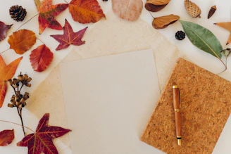 Autumn leaves surround a blank paper and pen.