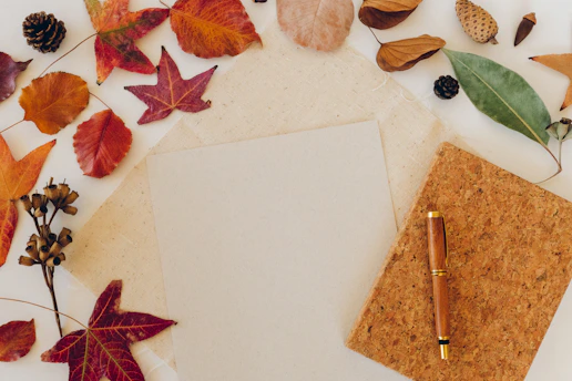 Autumn leaves surround a blank paper and pen.