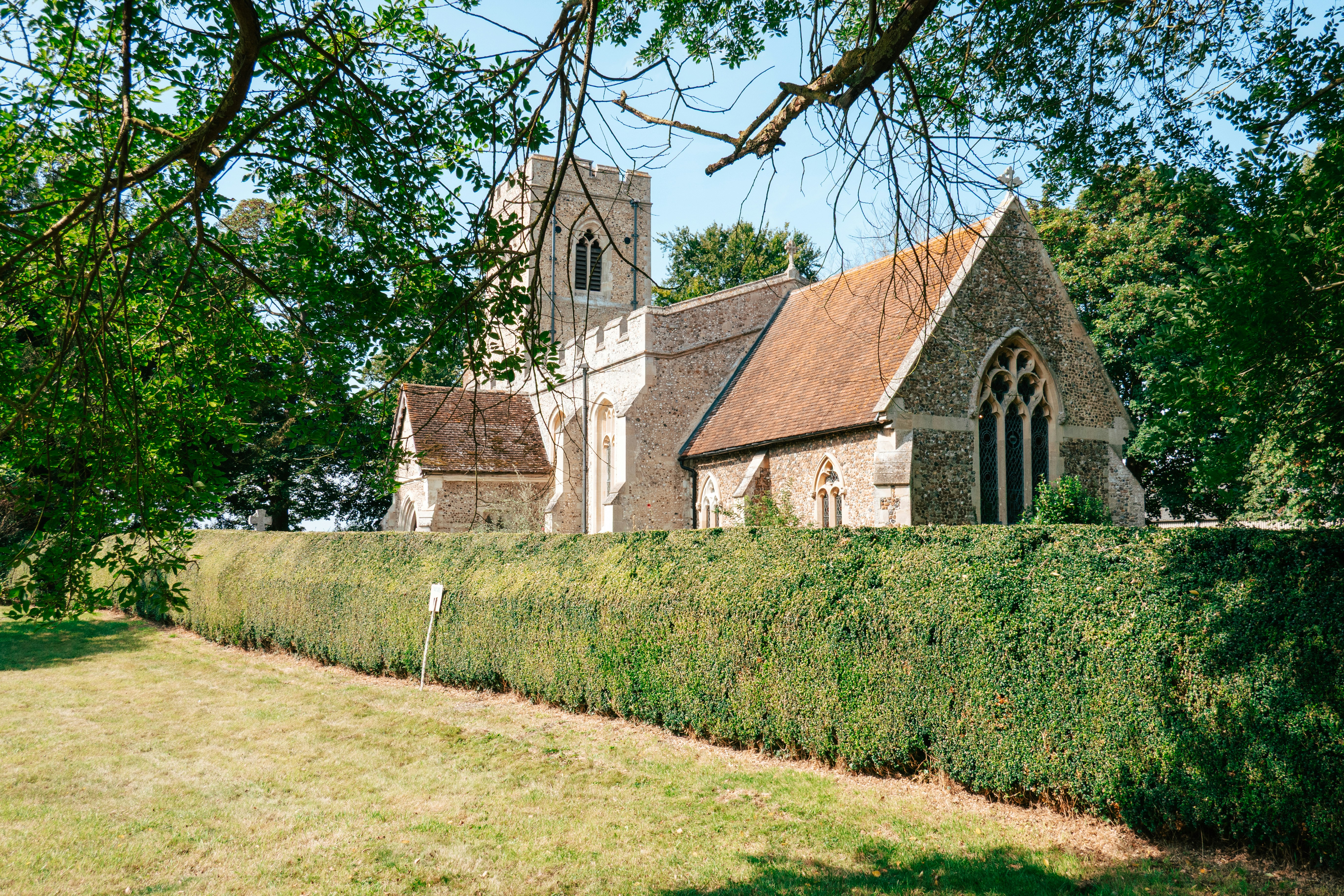 An old church rests amidst trees and hedges.