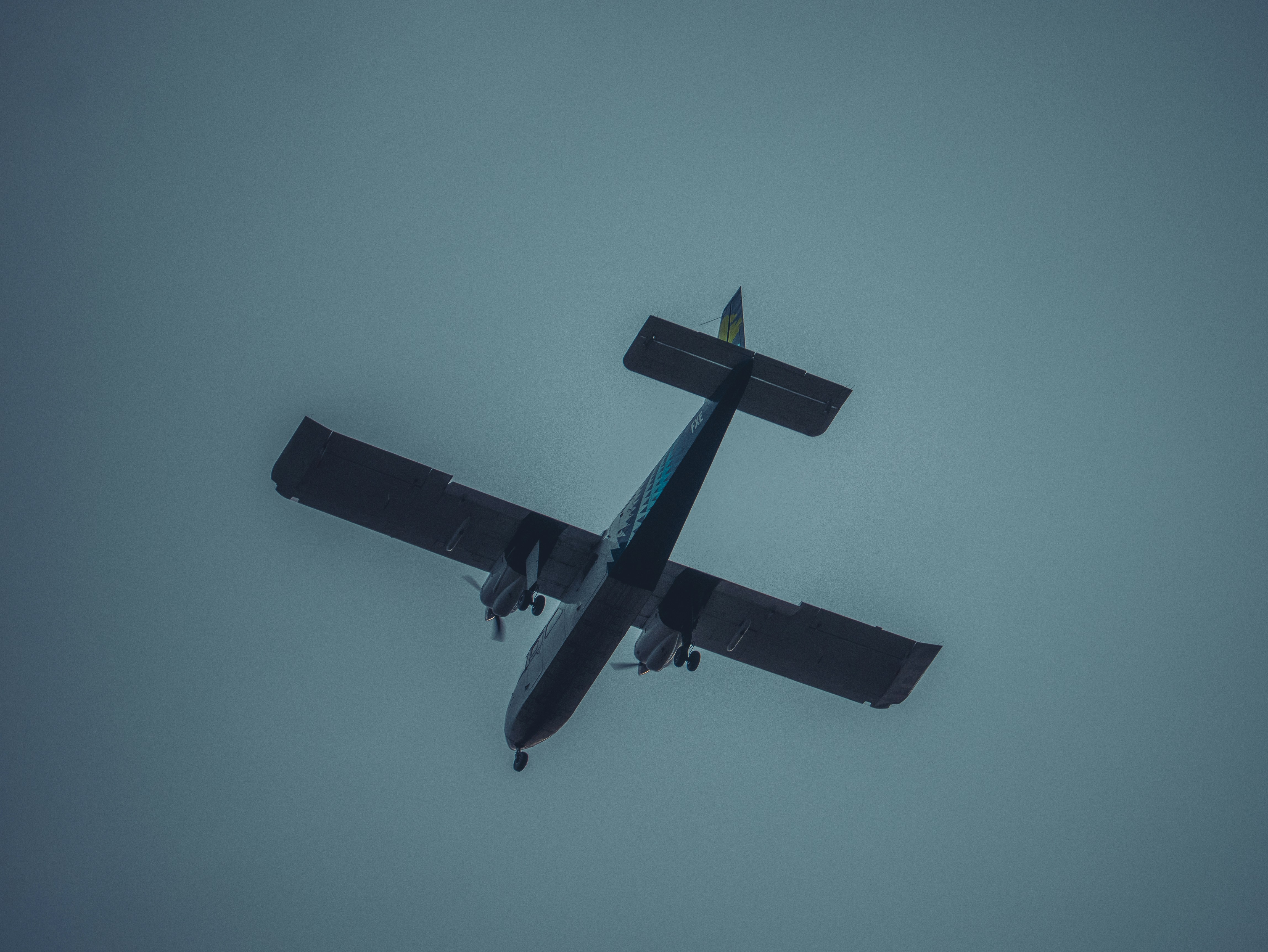 A plane flies against a gray sky.