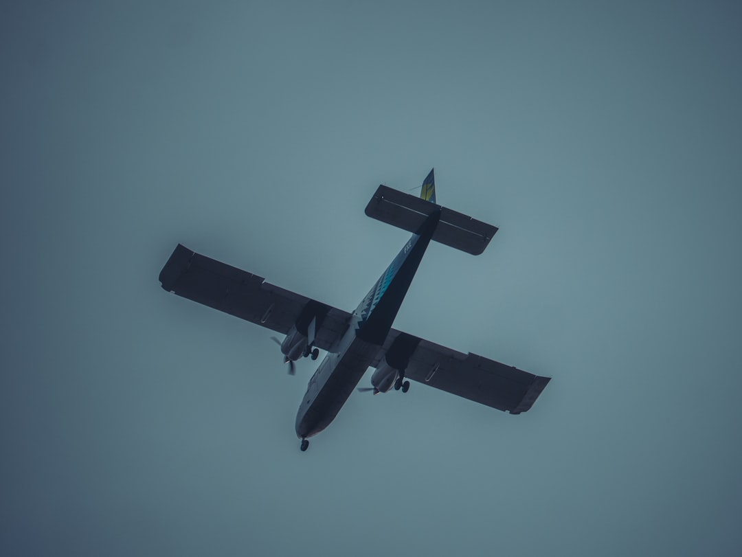 A plane flies against a gray sky.,
