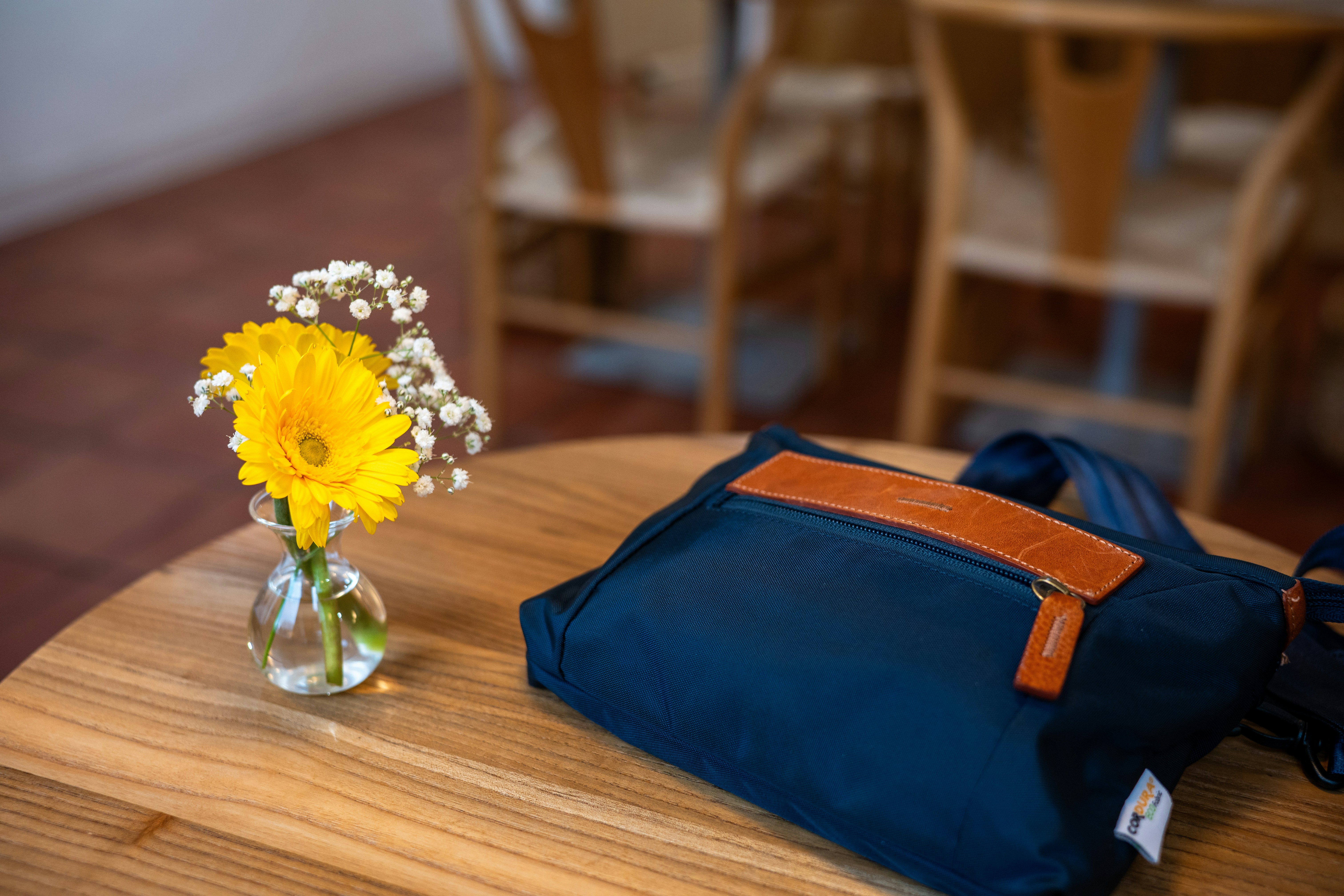 Flowers and bag sit on a wooden table.