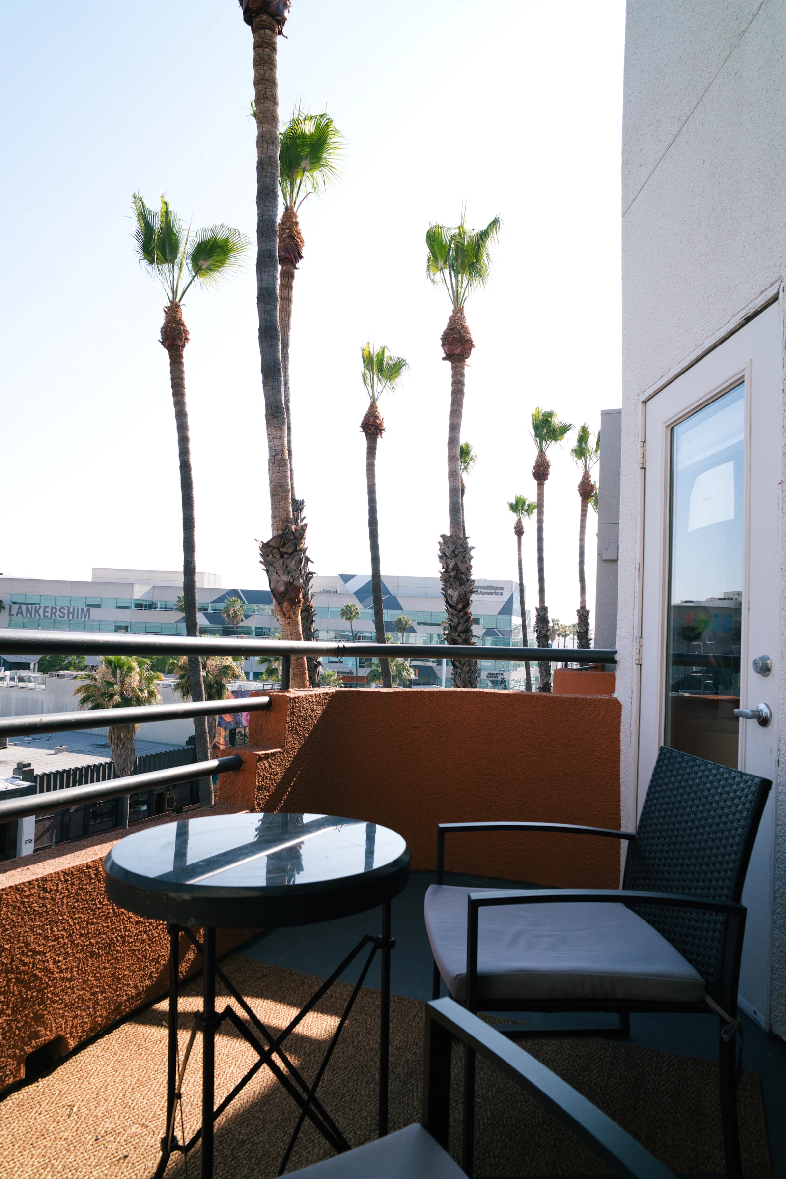 A balcony with outdoor seating and palm trees beyond